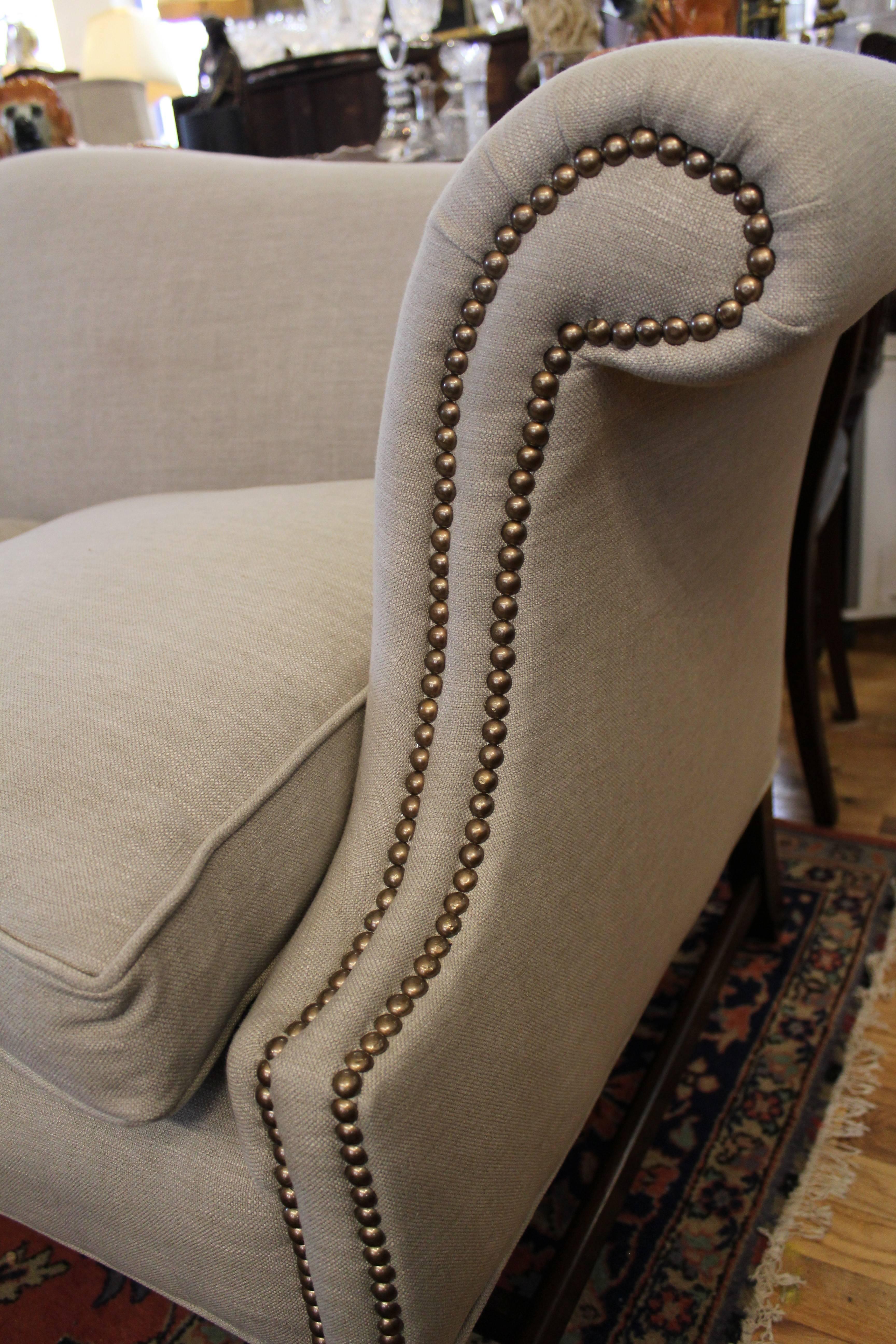 Antique Camelback sofa in the Chippendale style with Marlborough fluted front legs, scrolled arms with brass studded trim and down filled cushions all beautifully re-upholstered in a soft cream or beige fabric.

          