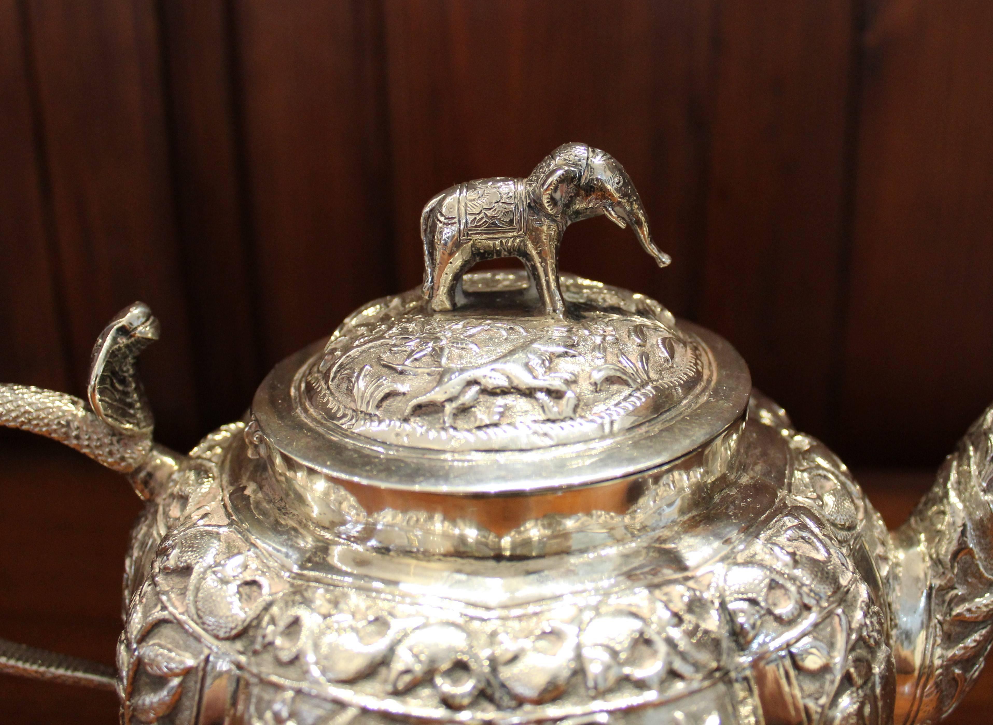Anglo-Indian sterling silver tea pot, cream and sugar bowl. This tea service is worked in brilliant répoussé and chasing. It features an array of animals, fish, foliage and figures throughout. The teapot has a richly detailed standing-elephant