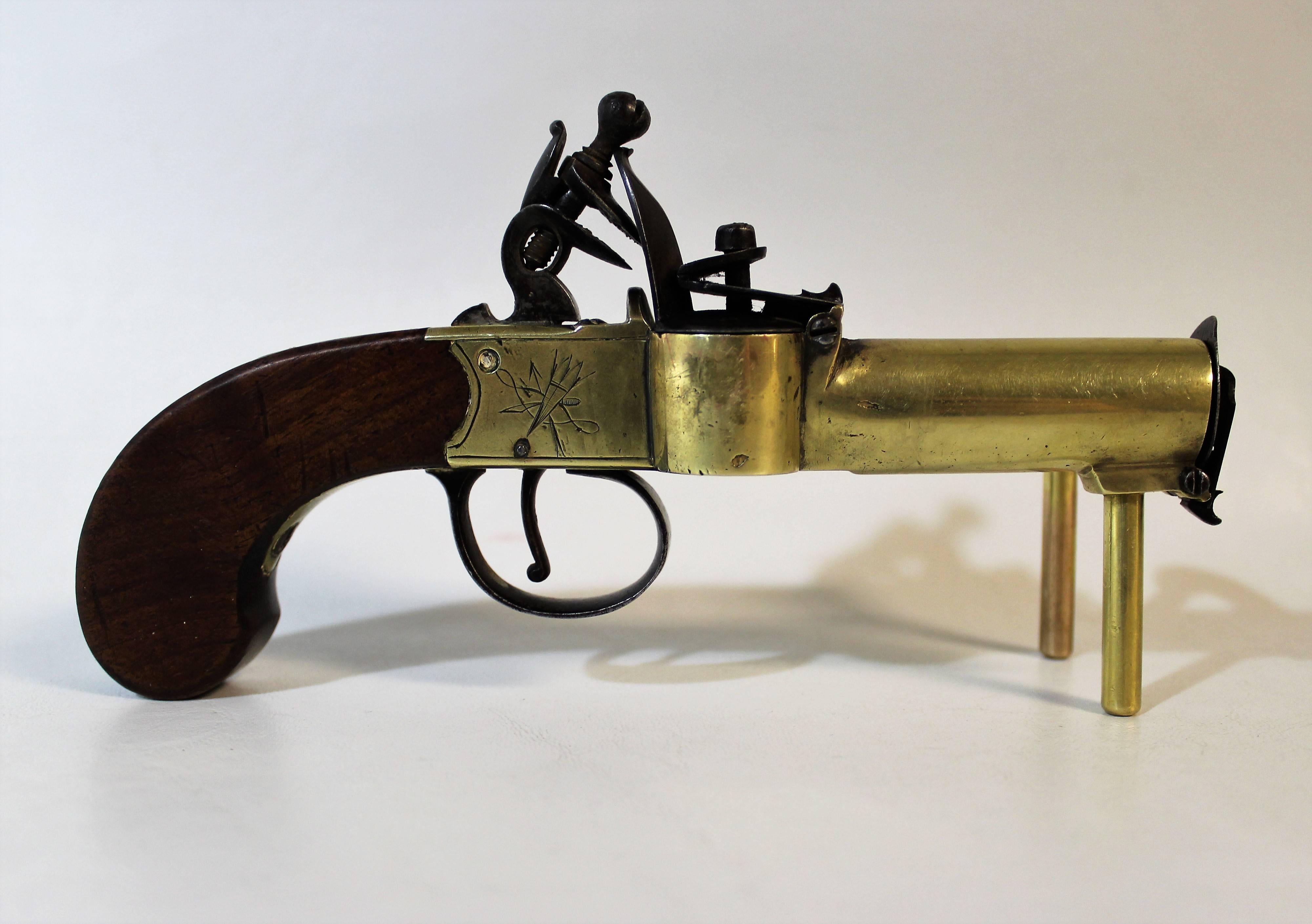 18th century, English brass framed and engraved tinder lighter in the form of a flintlock box-lock pocket pistol. The front of the lighter is hinged to contain tinder with a large central portion for ignition.
  