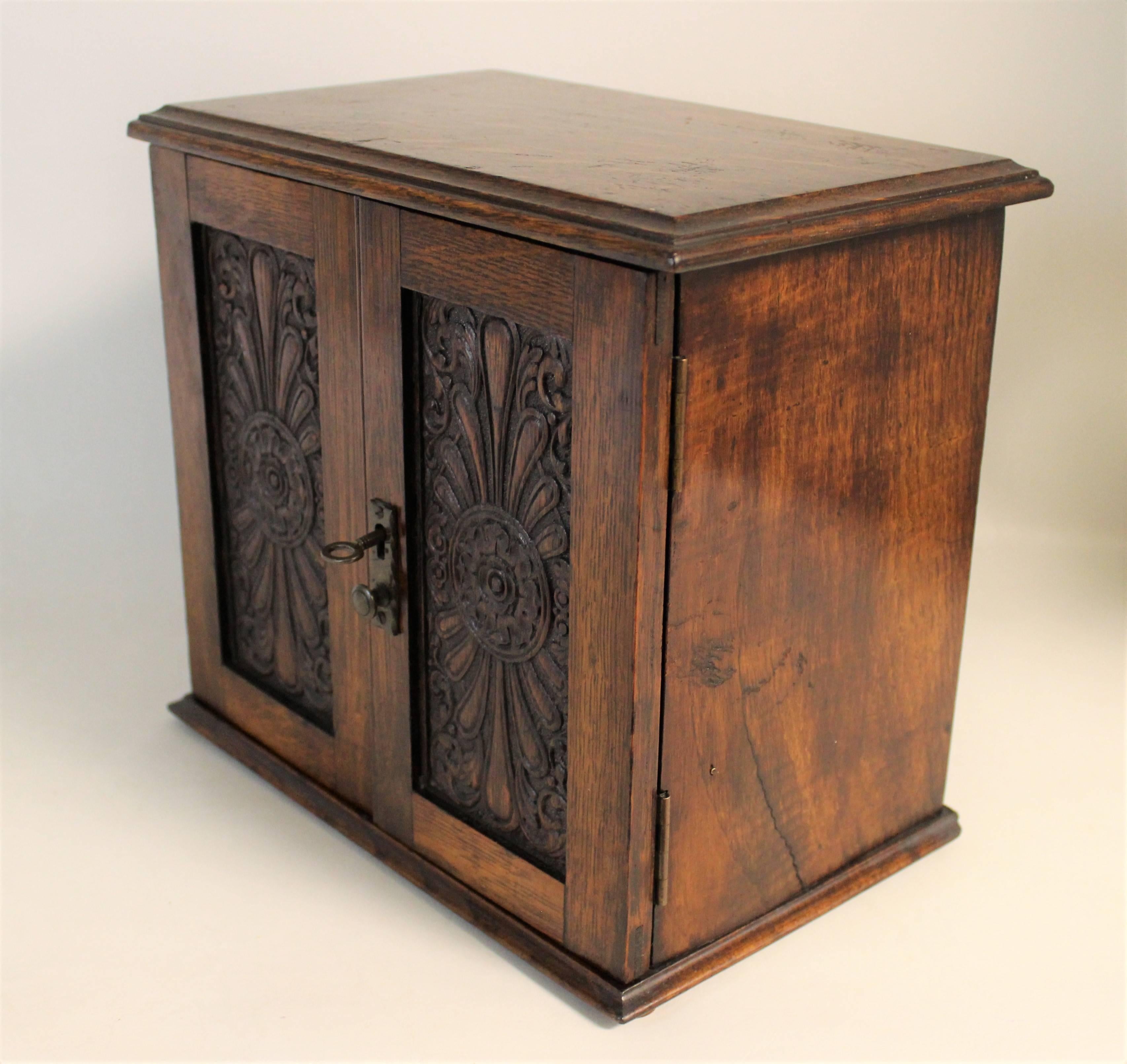 English Edwardian era smoking cabinet. This unique piece features two carved wood panels on the doors that pen to reveal a spot for your pipes, tobacco and cigars with two drawers for your tools and a flip-top lid that reveals an additional spot for