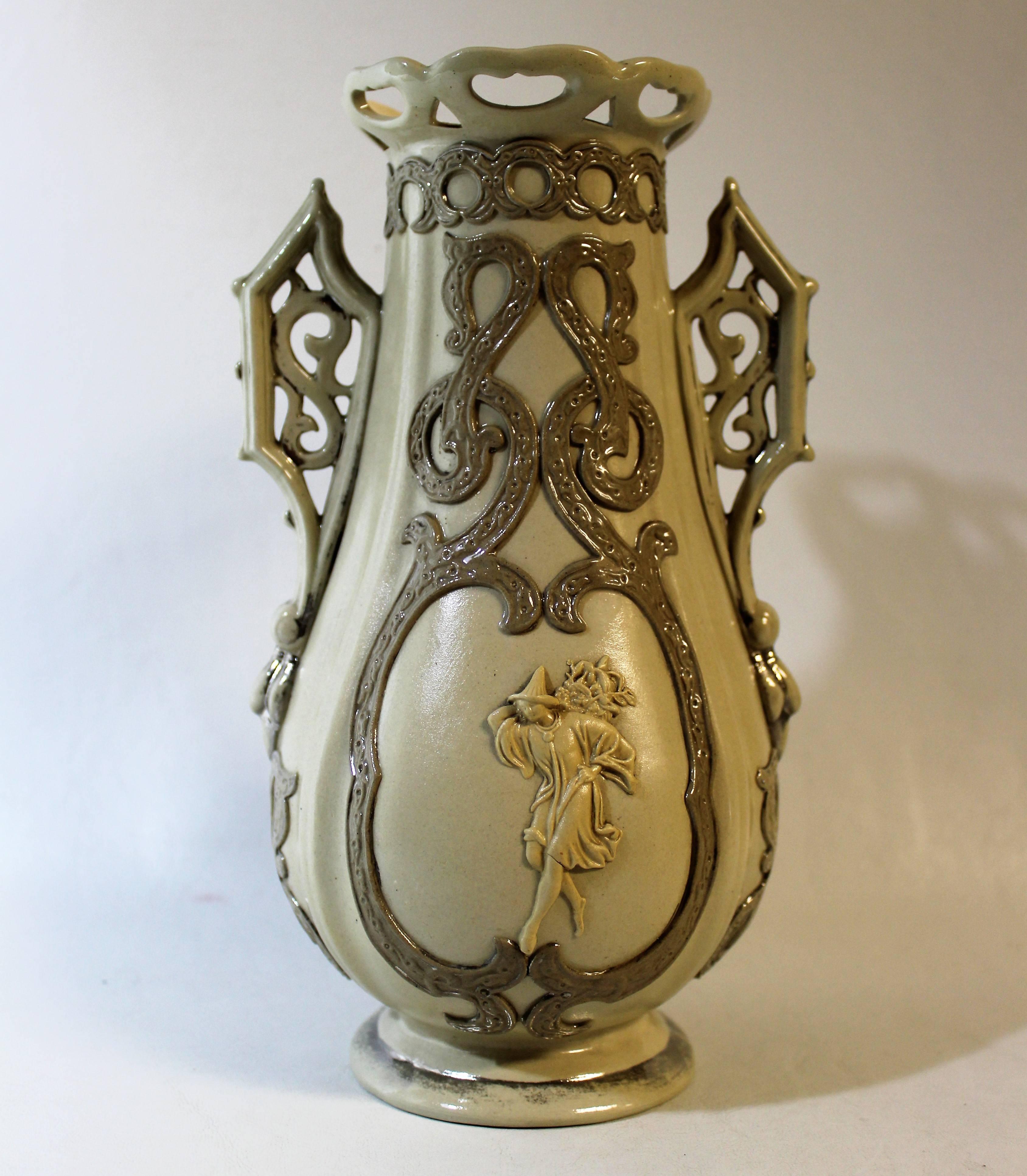 Antique ceramic vase made by Villeroy & Boch of Germany. This vase features four-tone Parian pottery with applied figures on each side and reticulated openwork rim and handles.

  