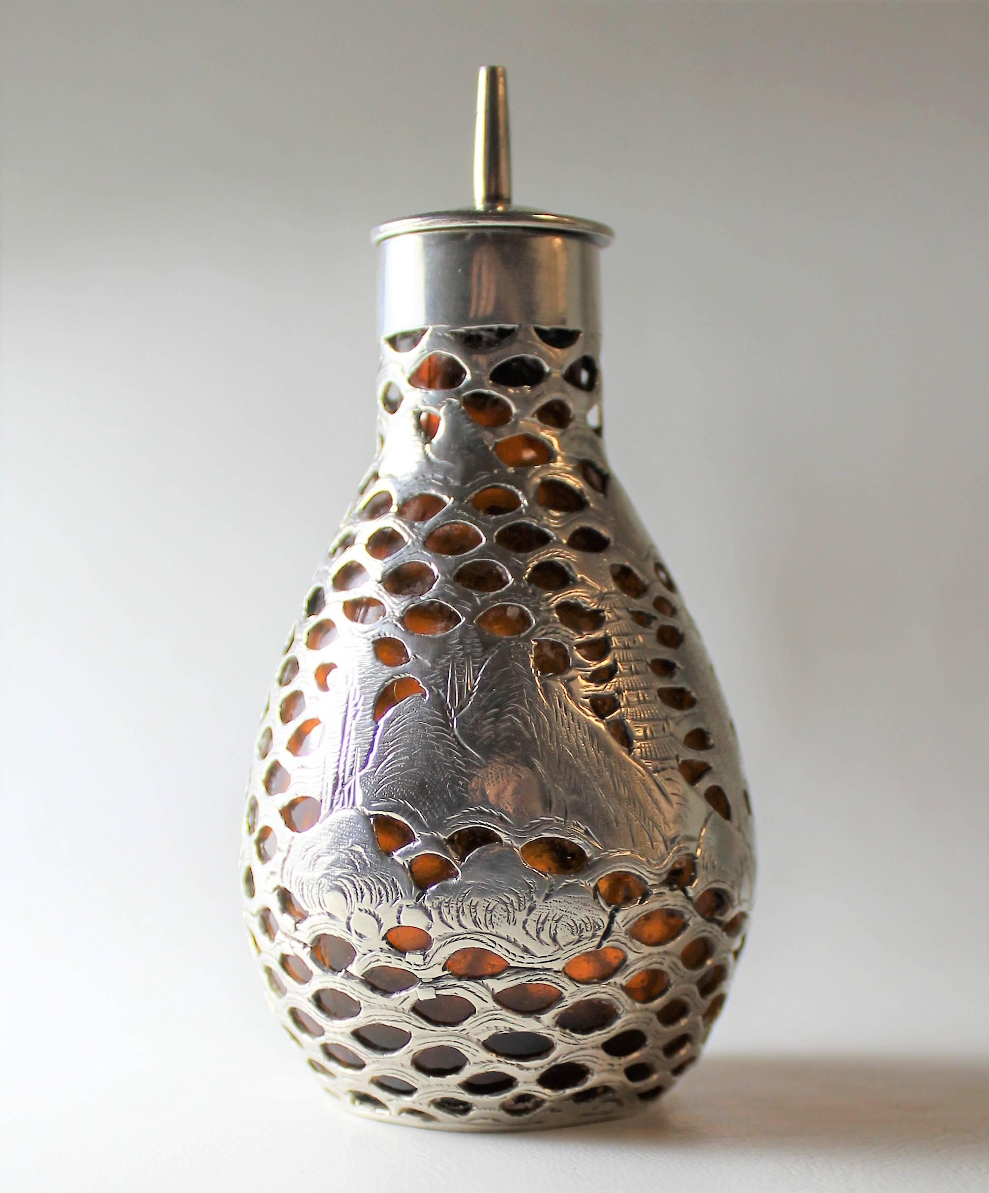 This beautifully made piece made by Wai Kee of Hong Kong consists of a Fine pierced solid silver cage surrounding an amber colored glass bottle. Both the silver and glass are marked as shown. The silver cage features an intricately hand chased