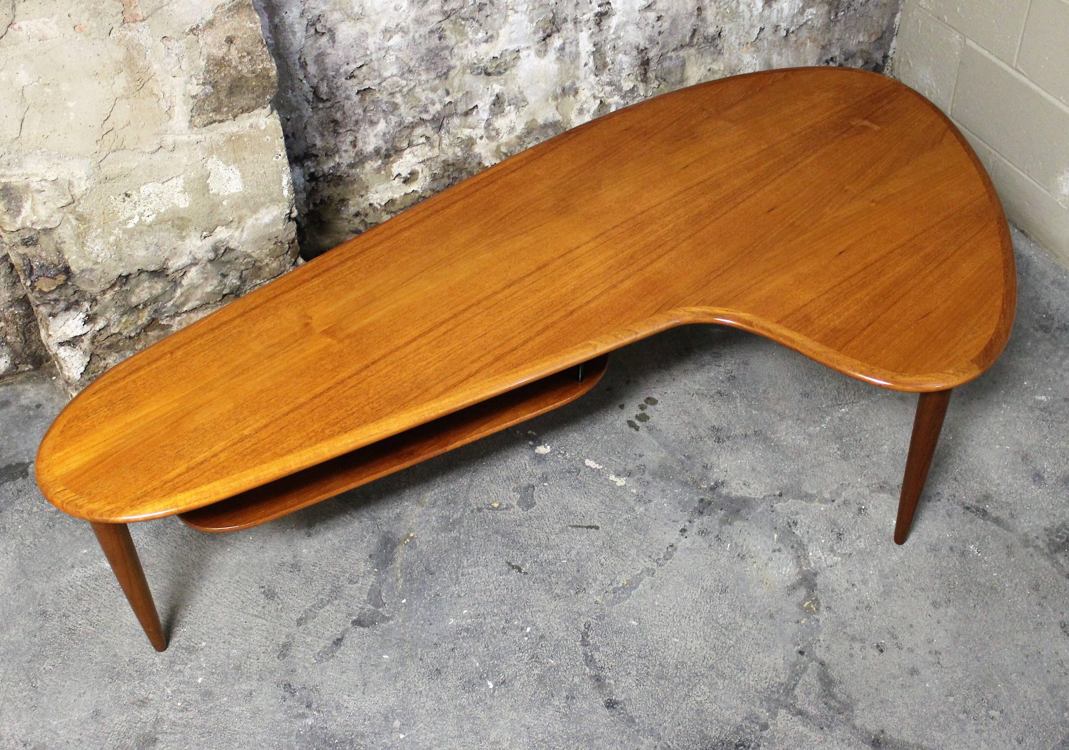 Gorgeously sculpted Danish teak boomerang coffee table. Scandinavian Modern take on this Classic design shape. It features a beautiful rich patina of from aged teak wood, rounded solid teak edges, tapered straight legs and a suspended magazine rack