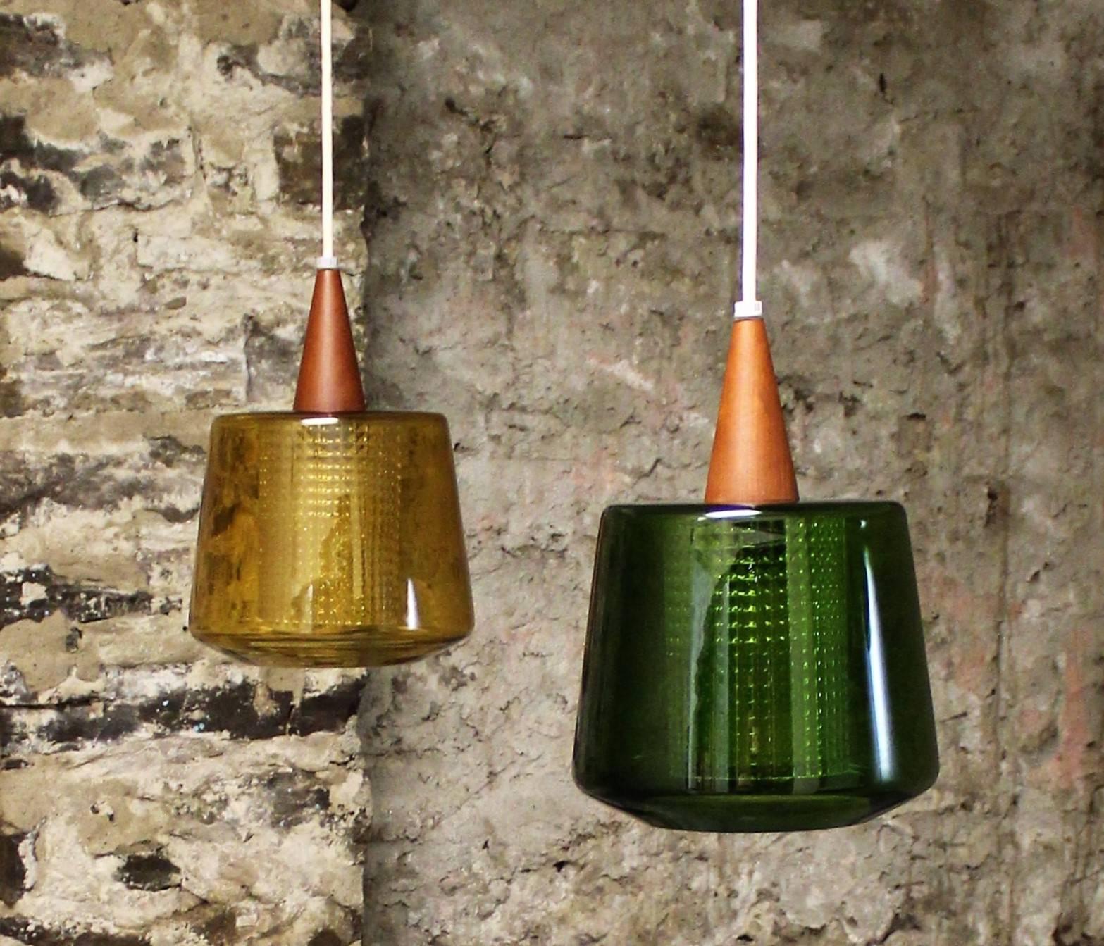 Pair of Carl Fagerlund pendant lights for Orrefors. One light shade is green while the other is amber. Each light has a teak wood fitting and clear patterned glass cylinders on the inside.

Scandinavian Modern, Mid-Century Modern.