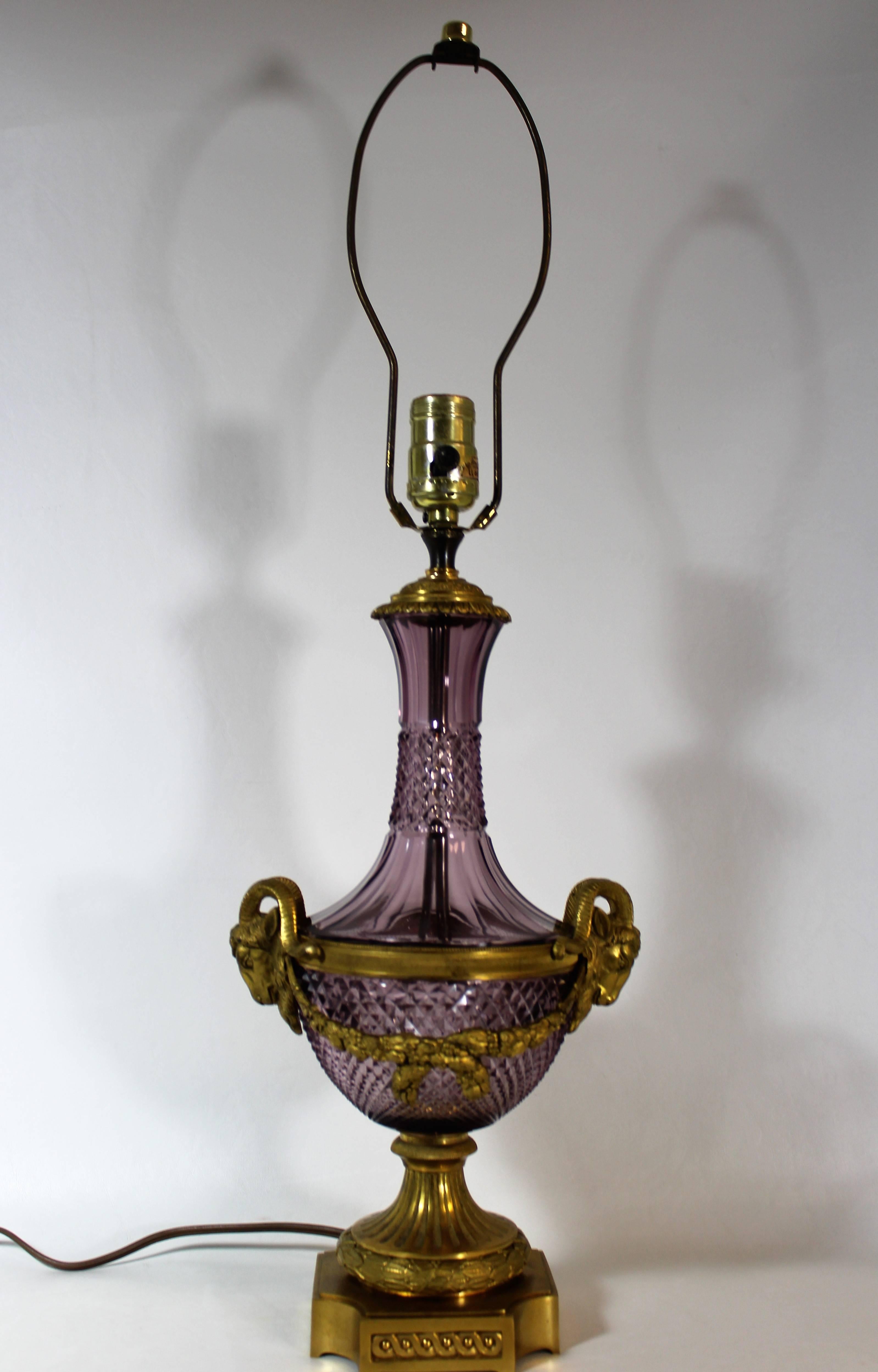 Elaborate Austrian bronze ormolu adorns this pair of amethyst crystal Baccarat lamps. Each lamp is beautifully decorated in the Classic French Louis XVI style, with gilt bronze rams heads and floral swags flanking each side. Boasting a complex cut