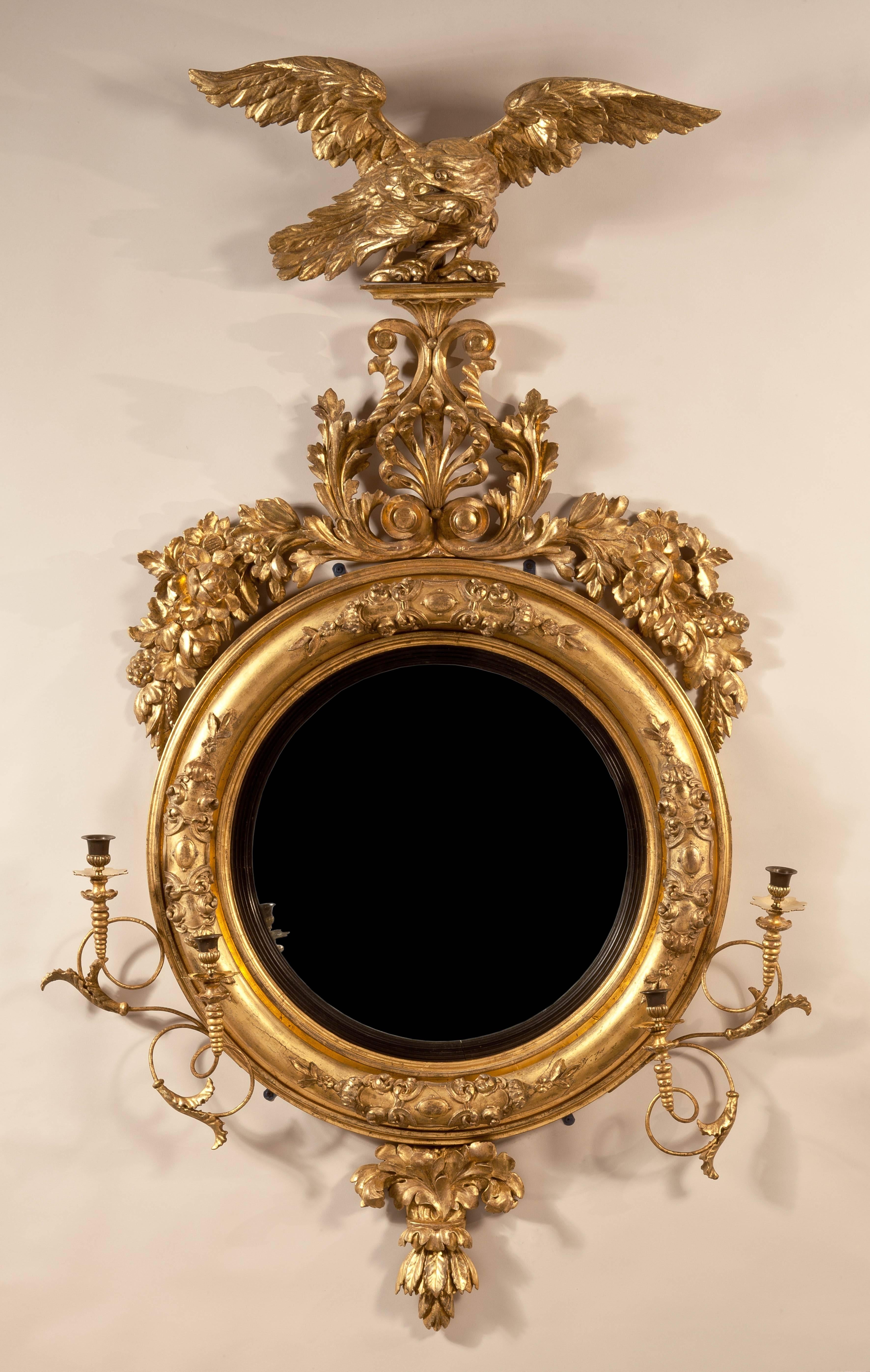Surmounted with an Eagle and Anthemeon.
American or English, circa 1825.

A carved eagle with spread wings on a tapering platform above scrolled foliage and a pierced anthemion above a convex glass surrounded by an ebonized mirror slip and gilded
