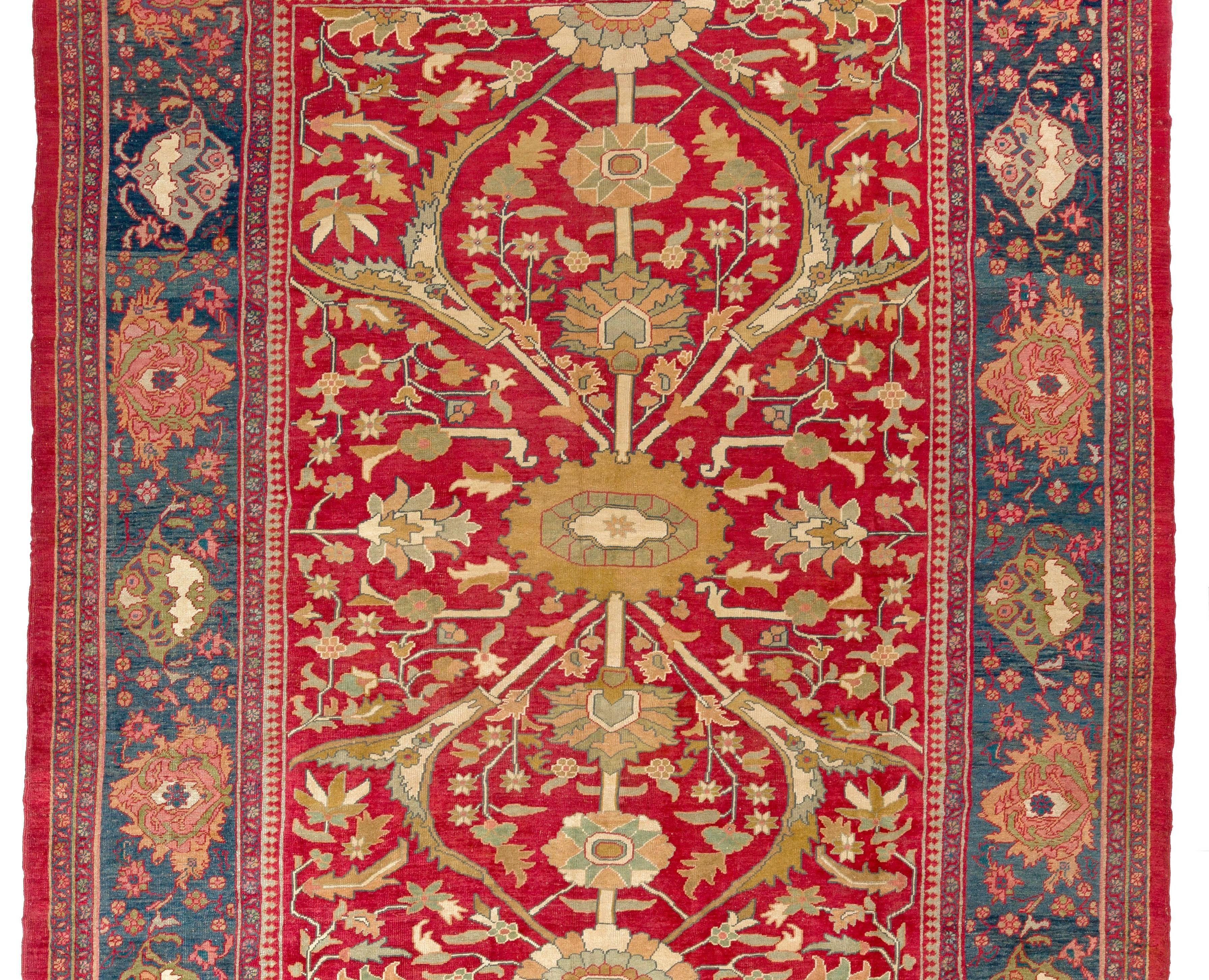 This striking Persian Ziegler Mahal Rug has a vivid red field featuring angular leaves and floral vines with a rather simple olive green blossom at the centre that also forms an axis of linked large palmettes and rosettes running halfway through the
