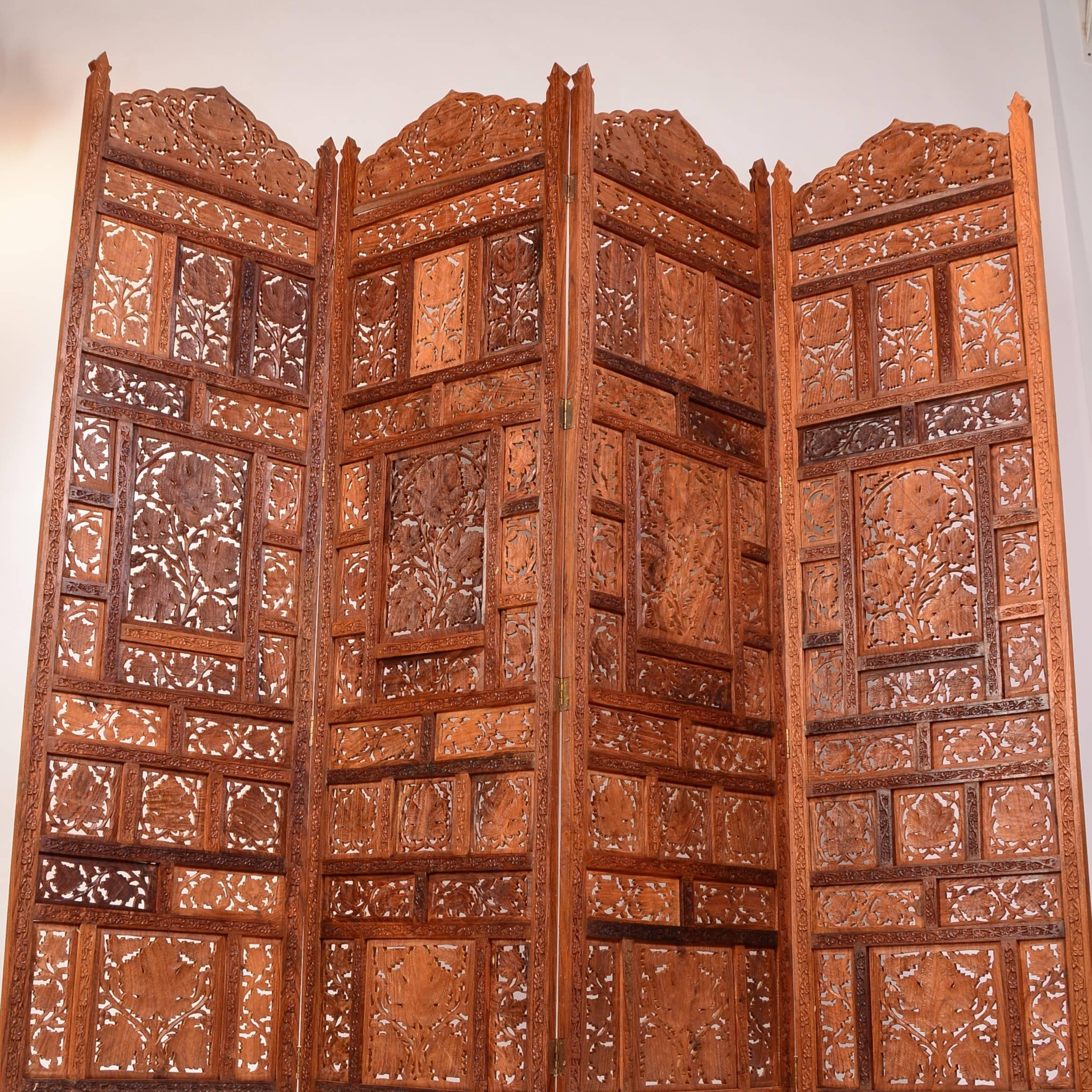 We have four of these beautifully preserved Anglo Indian elaborately carved four panel screens in stock. circa late 1800s, these heavy teak folding screens feature elaborate open work carved panels with leaf motif. The listed price is for one 4
