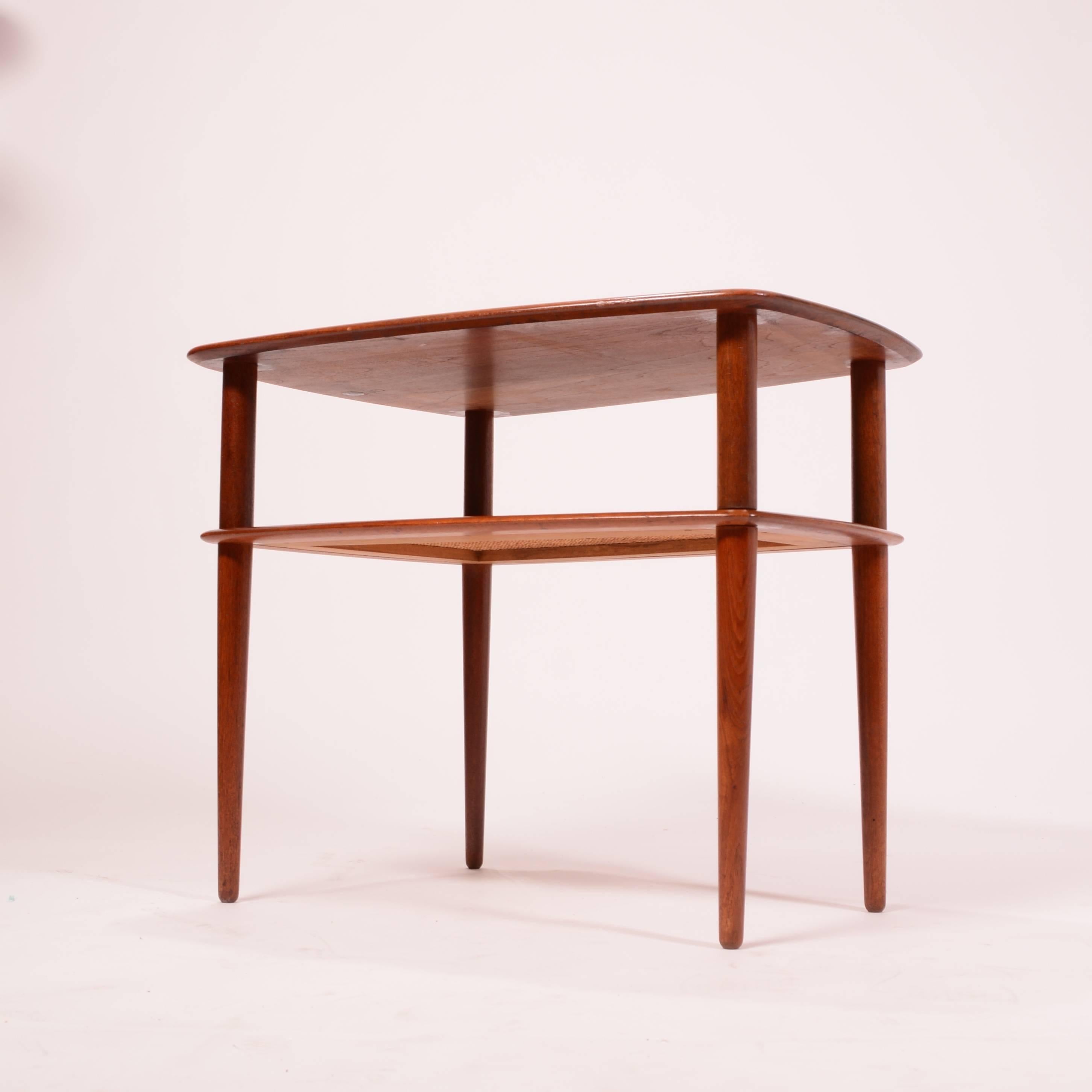 This is a great side table by the great danish designer Peter Hvidt. Richly grained solid teak. Lower caned magazine shelf.   This table dissembles for easy shipping.  In excellent condition.  
