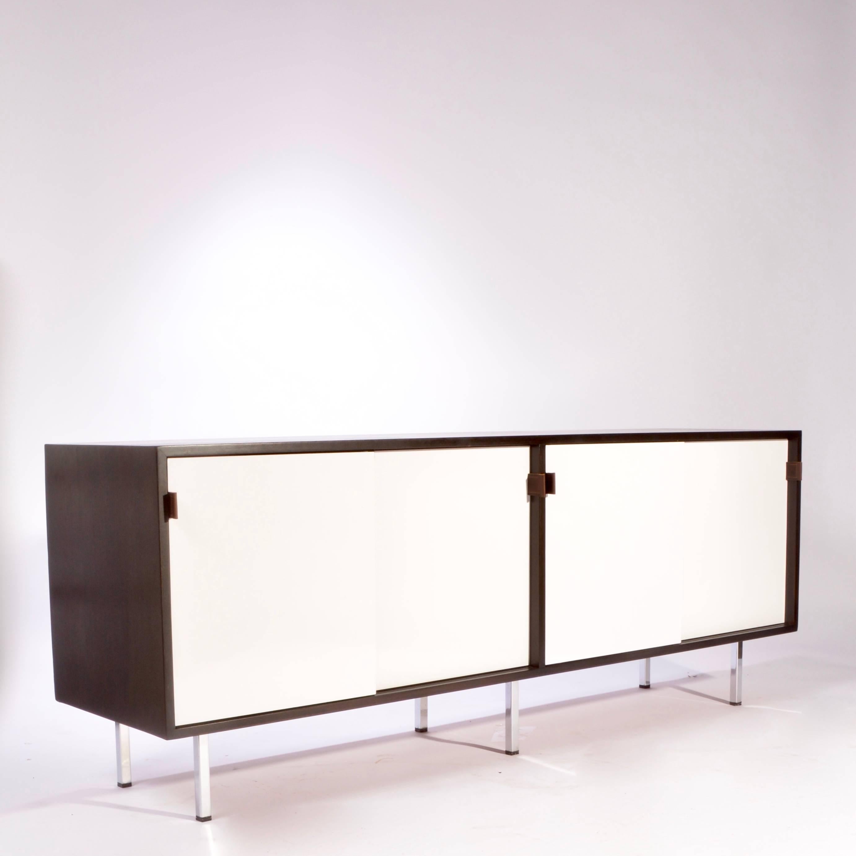 This is a fully restored early Florence Knoll credenza featuring white formica sliding doors, new professional ebonized finish, brown leather pulls, chrome legs and solid oak drawers. We have two in stock and can offer a range of interior options