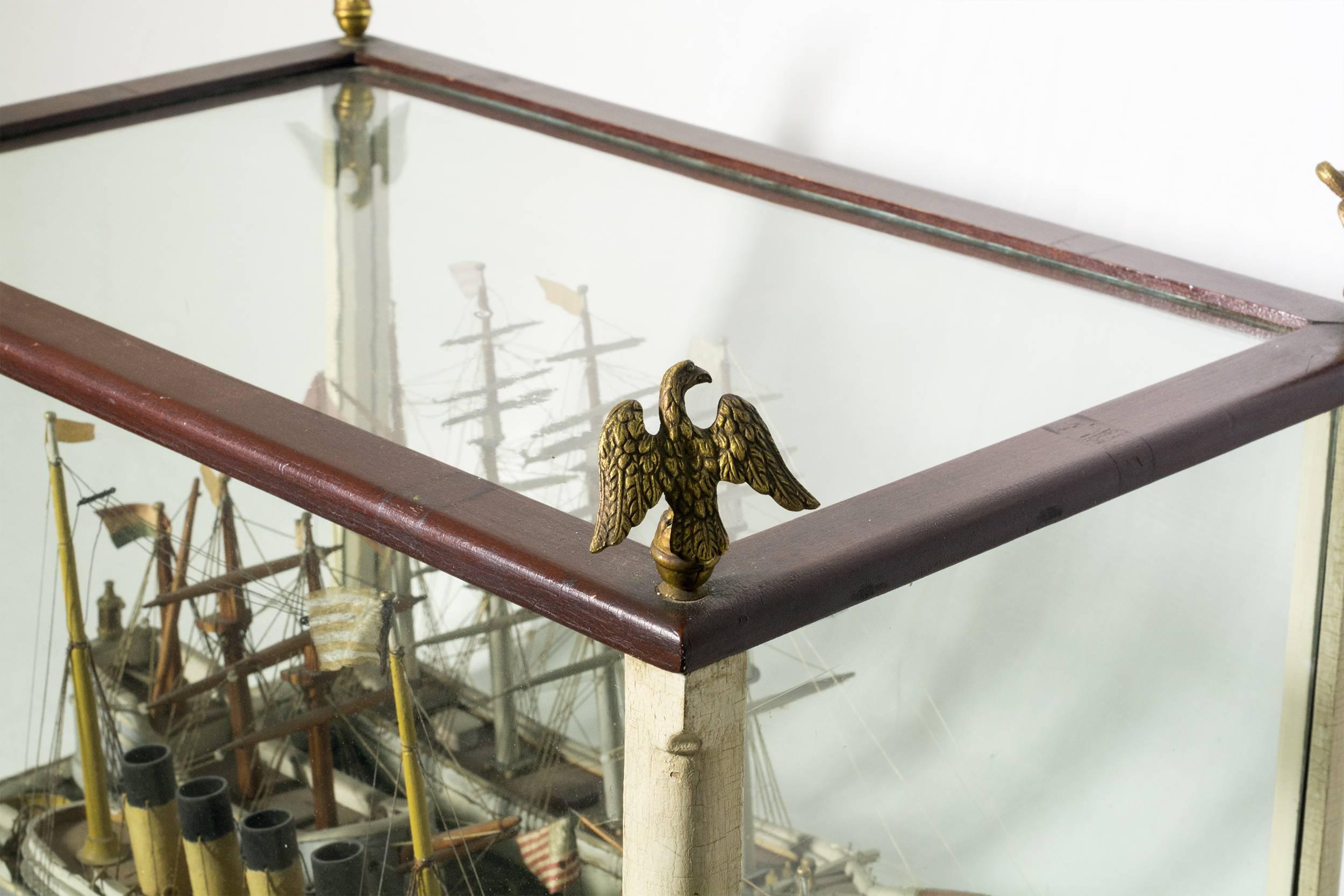 The diorama has four different ship types, with both American and England vessels, mounted on a molded putty sea. The case is painted and has four brass eagle finials.