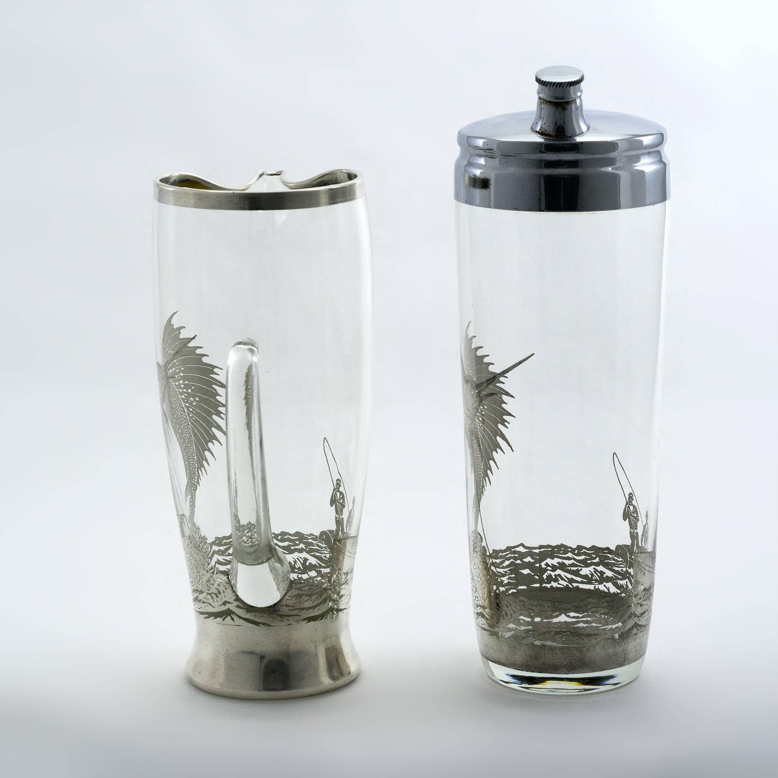 1950s cocktail shaker and pitcher
in clear glass with silver overlay.
Each piece with a large sailfish leaping from 
the waves on the front while the back has a
fishing boat with fishermen. The handled pitcher
has a silver overlay rim with a
