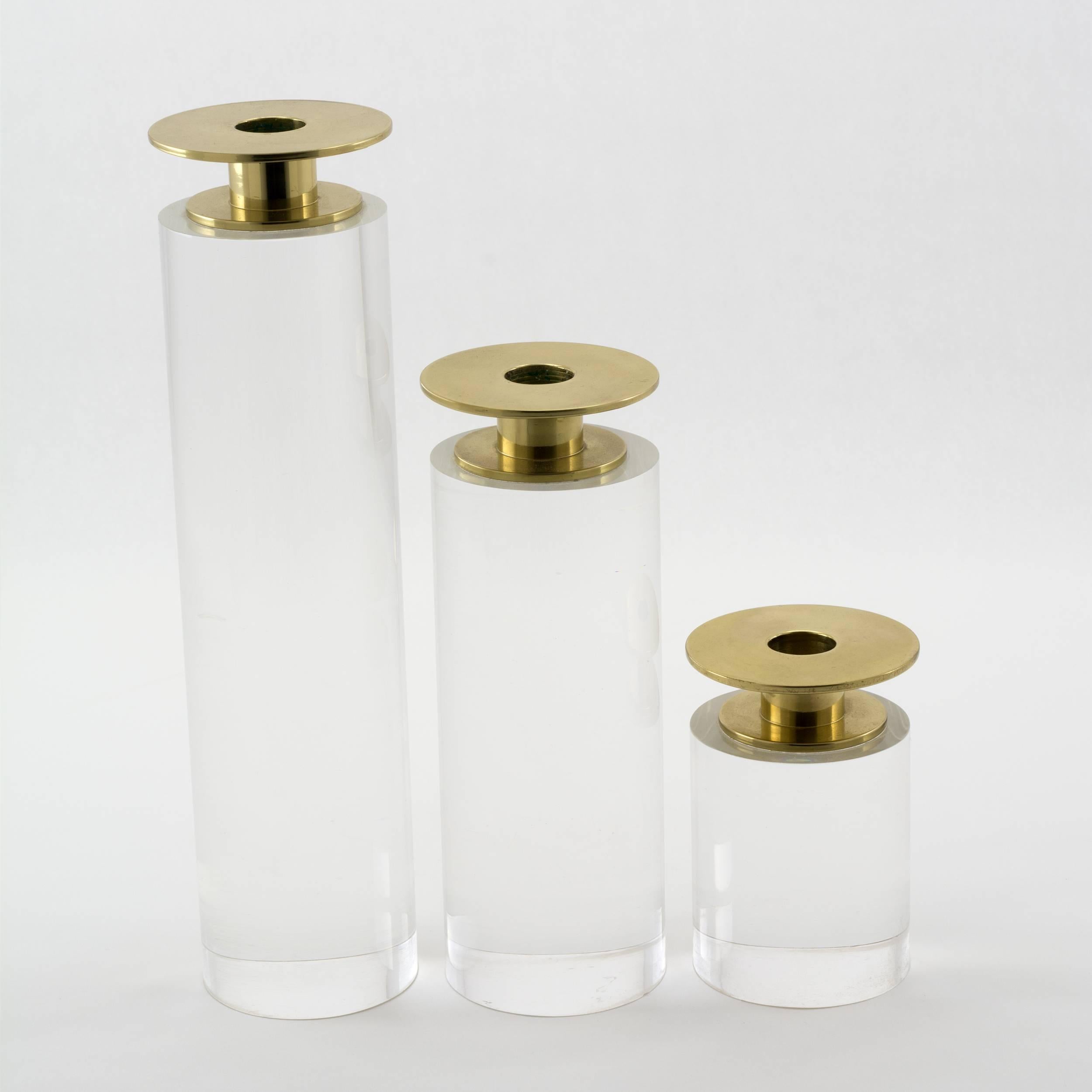 A trio of graduated candleholders by Karl Springer.
Each solid pillar of clear Lucite topped by a brass disk
supporting the candle cup which is topped by another disk
of equal diameter to the pillar.

Measures: 10-1/2”, 71/2” and 4”tall x