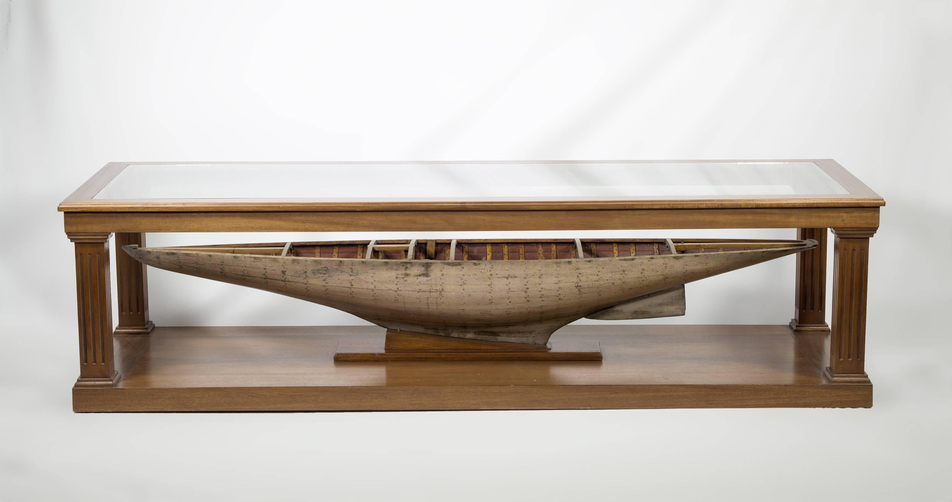 The coffee table has a recessed glass top and is bench made out of mahogany with fluted columns. The antique English pond yacht model is affixed to the bottom and bears its original white painted hull.
 