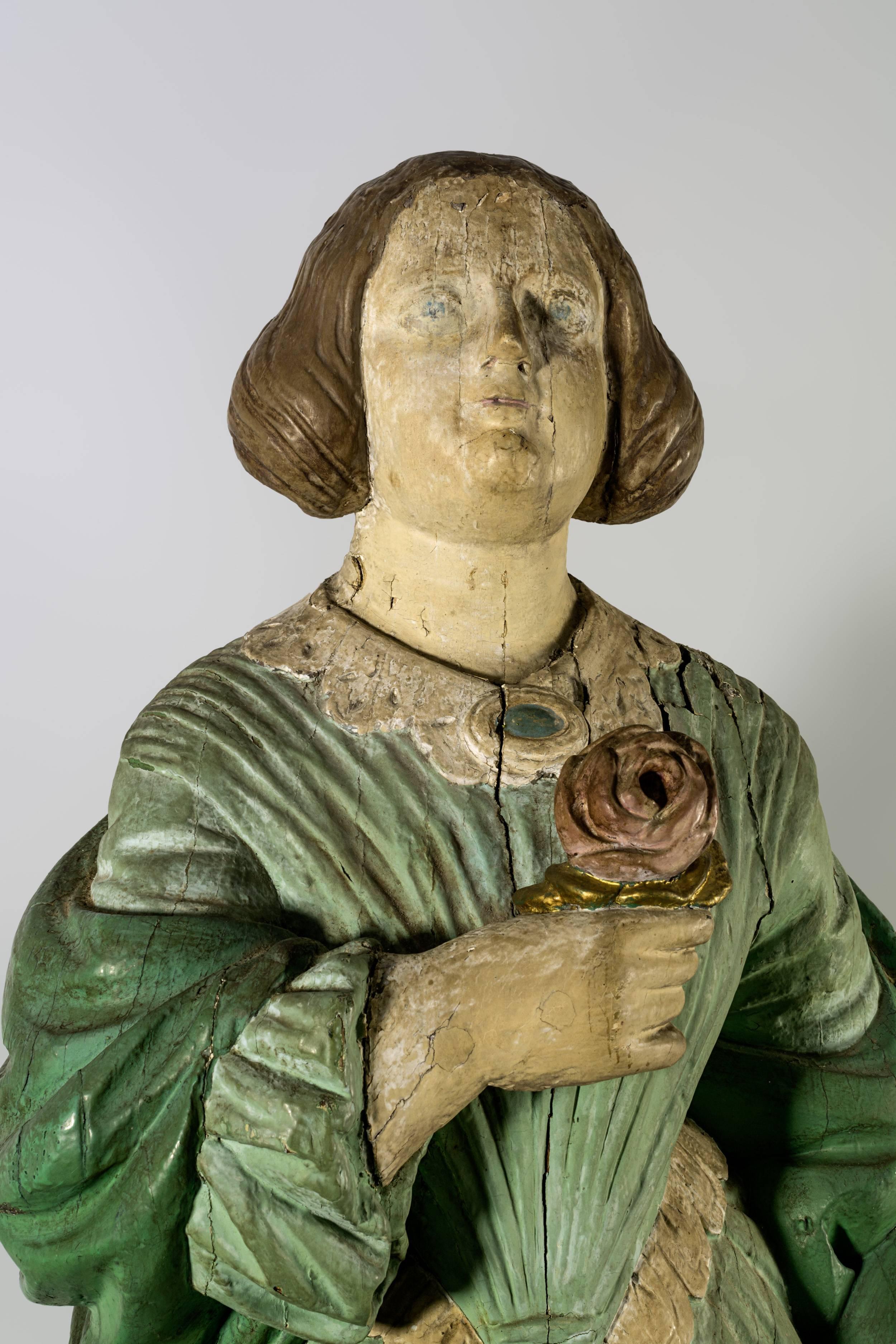 A carved and painted full length ship’s figurehead of a young classical woman dressed in green, with oval brooch necklace, holding a rose. Carved from a solid piece of pine.
English, c,1850, 37 ½”.
 