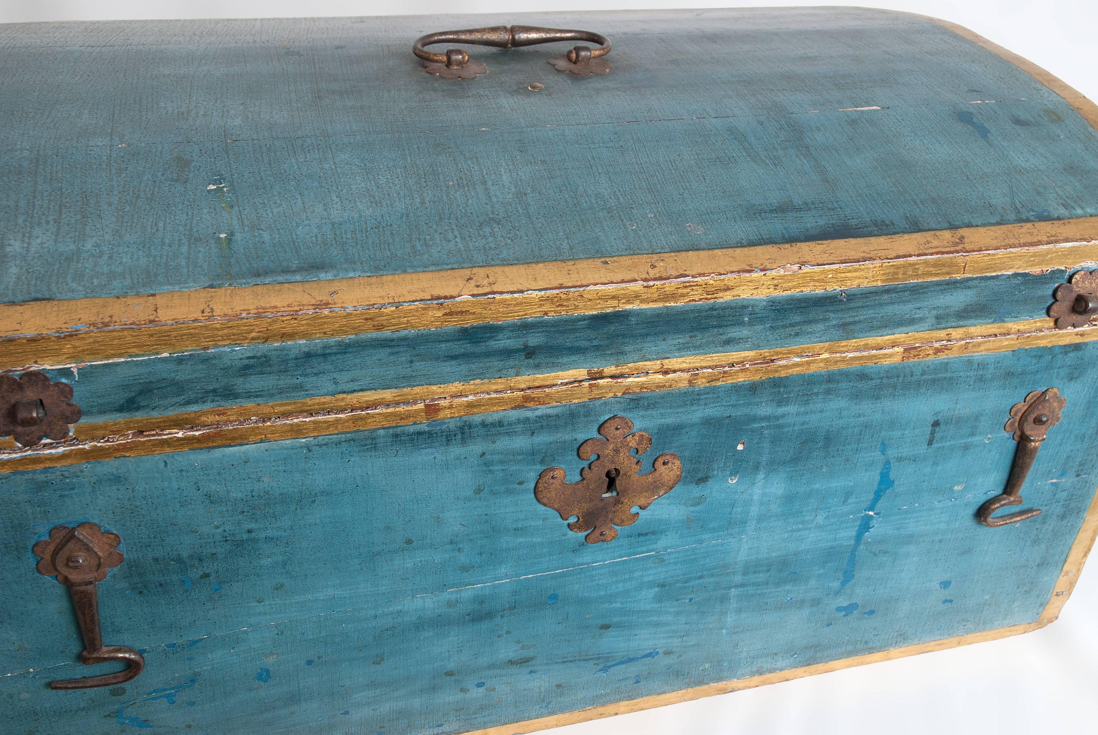 A blue painted and decorated wooden dome-top chest with yellow and gold border and bail handle and decorative escutcheon and double latches.
The interior has the original silk liner