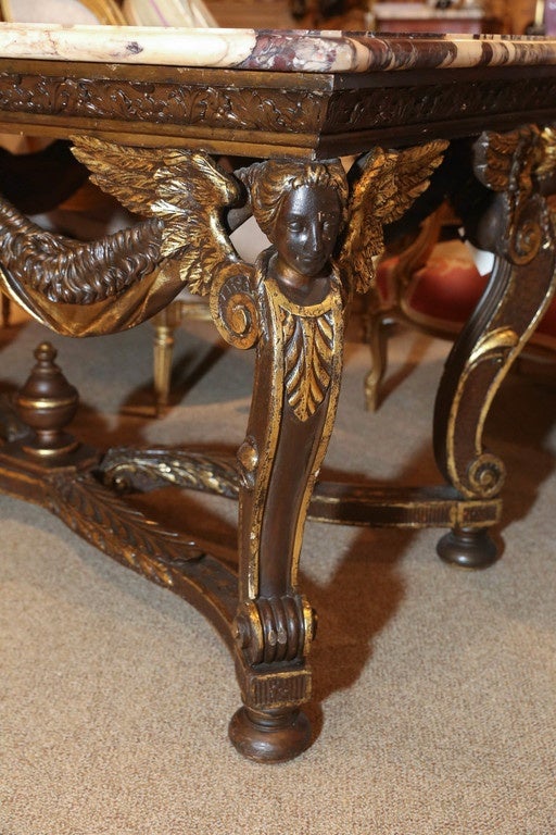 Beautifully carved center table
Winged Angels carved on a serpentine leg ending on a
Half bun foot

Breche de violet marble 
Carved foliate apron
High lighted with gilt accents

Carved stretcher culminating at the center with a