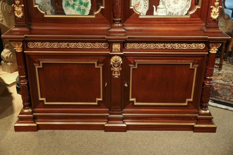 Triple breakfront rectangular cornice  above a paneled frieze of scrolled bronze work in highly gold gilded hue.
Centering a classical mask with blossoming cornucopia over a fluted
Corinthian colonette flanked by beveled glazed doors opening to