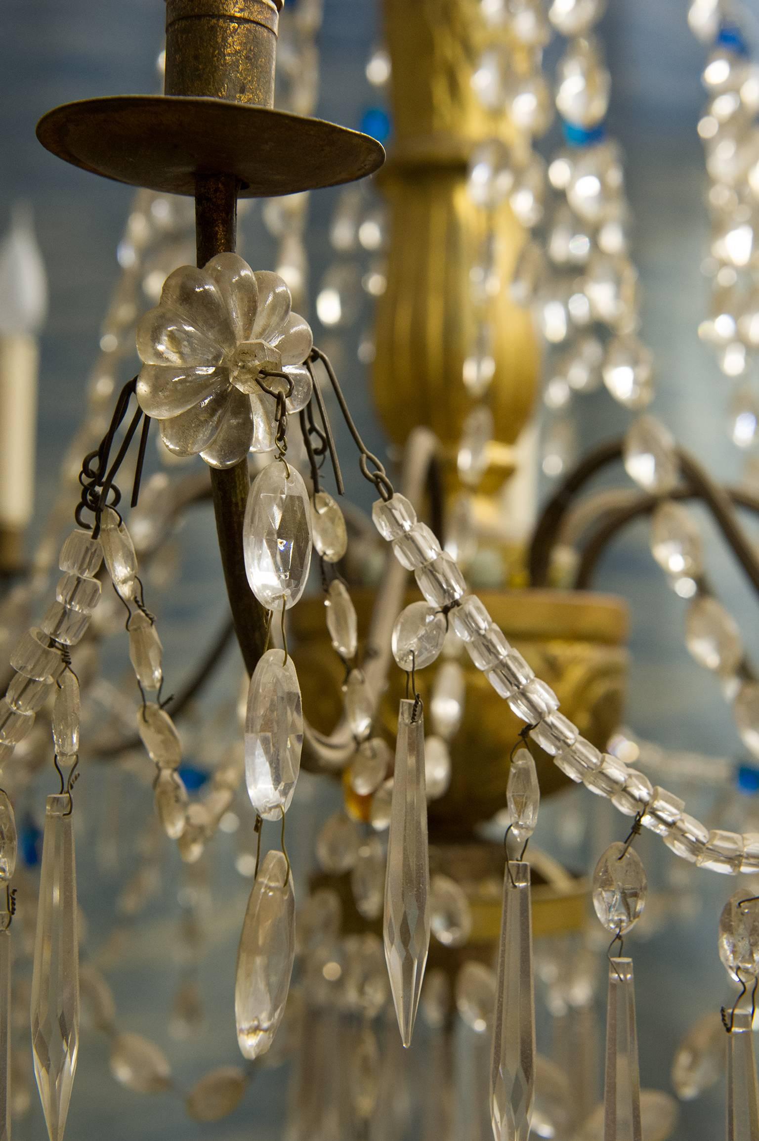 Antique authentic Genoese chandelier, with crystal drops, even colored and finely carved gild wood, perfectly restored.  Like this:  into Palazzo Ducale in Genova. Note the central rod in gilded wood, not metal ! Eight lights.
In the most glamorous