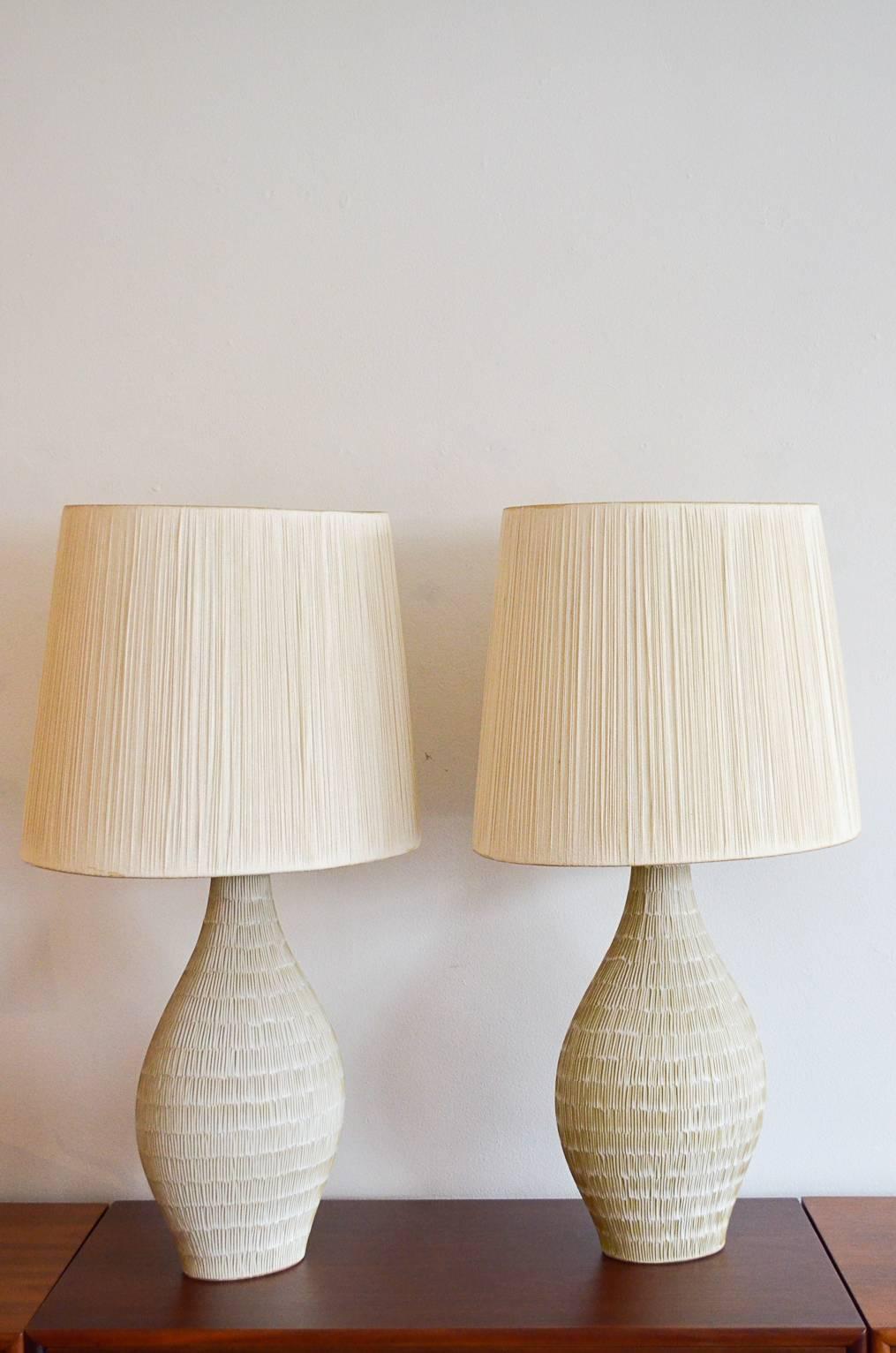 Elegant pair of large cream or ivory ceramic lamps with incised pattern. Beautiful shape, original oval string shades in excellent vintage condition. Original wiring. Lamps measure 20