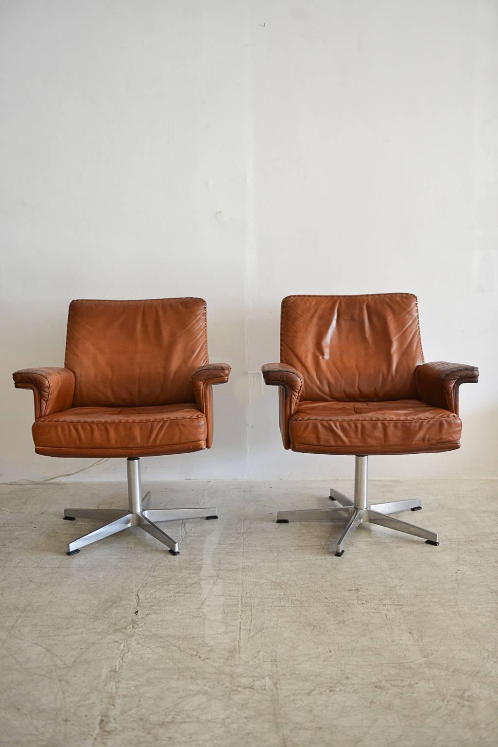 Luxurious saddle brown leather stitched swivel armchairs by Swiss manufacturer De Sede. Wonderful, rich patina to the leather, in very good condition, in as found condition from the 1960s.

Swivels are stabile, no sticking or extra play and the