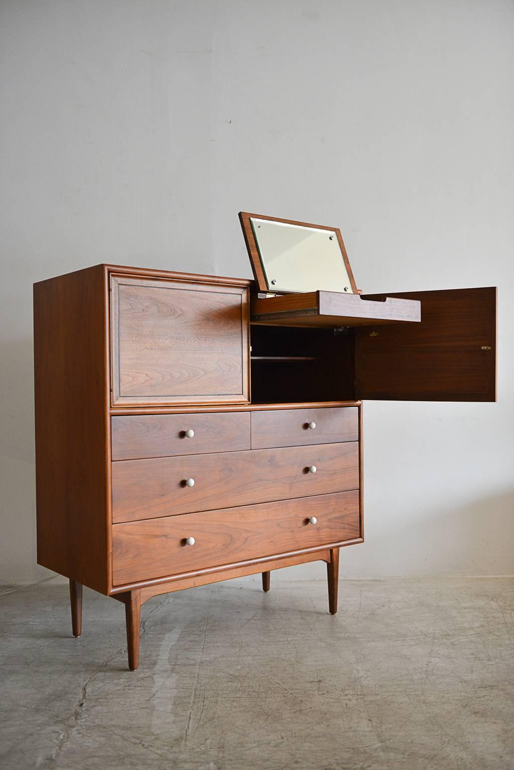 Fully restored gentlemen's highboy dresser by Kipp Stewart for Drexel Declaration. American walnut with original porcelain hardware. Upper half opens to reveal sliding drawers on left and a pull-out mirrored drawer with built in dividers on right