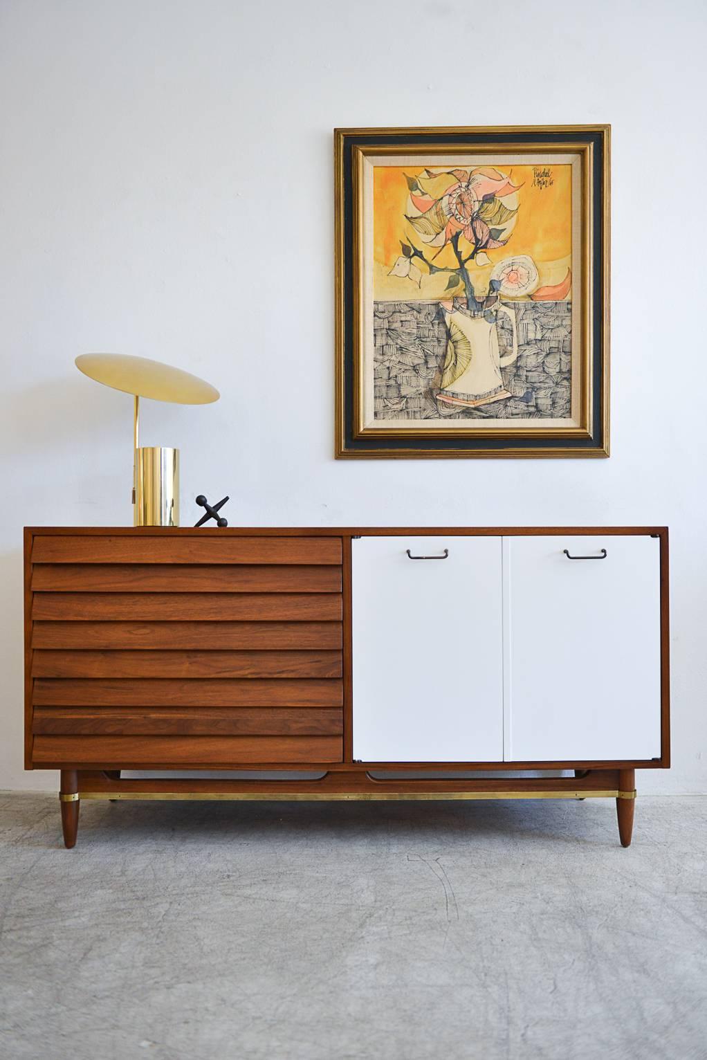 A new twist on an old classic, this beautiful walnut and brass dresser or credenza by Merton Gershun for American of Martinsville has been fully restored and updated with white front cabinet doors that match the original white inside drawers and