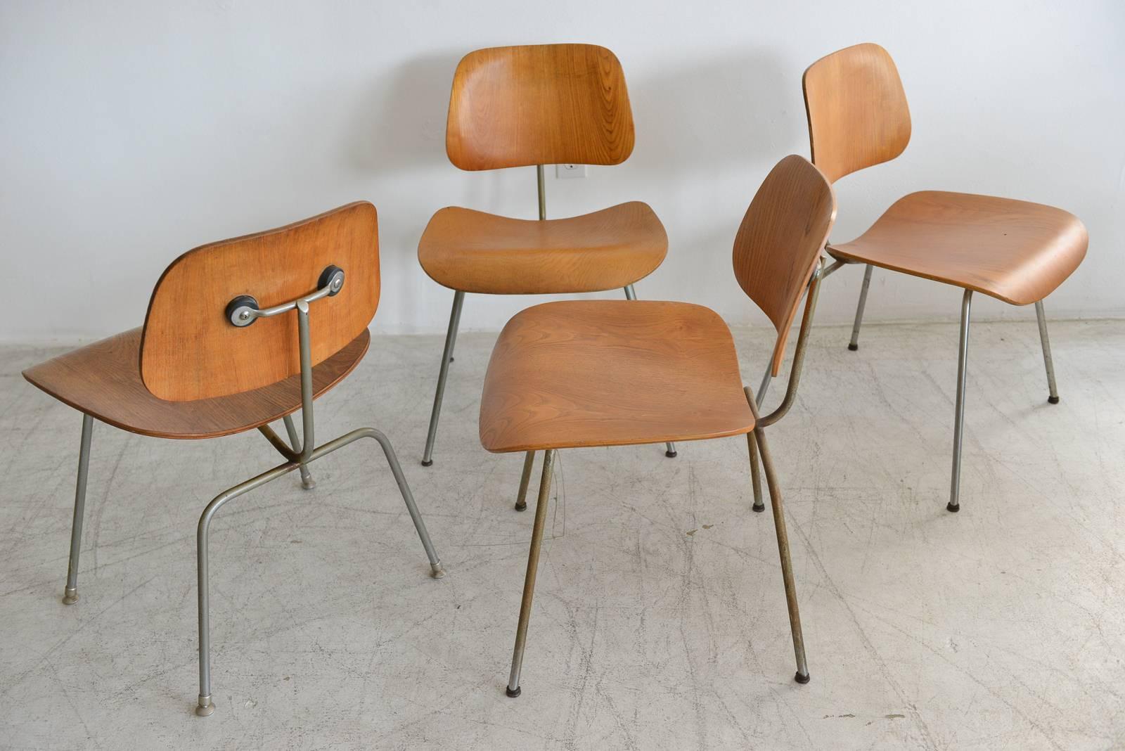 Set of four Charles Eames DCM dining chairs. Two have original early first edition labels, one is unmarked and the other has older foil label. Original shock mounts in good condition, frames have patina. Wood is in good condition, see photos for any