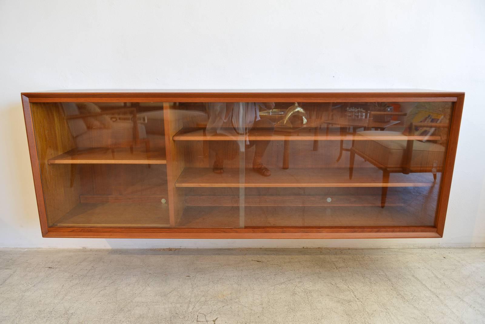 Teak wall-mounted Floating Cabinet by Gunni Omann, circa 1960. Includes two sliding glass doors and four adjustable shelves.

Could be used as a media cabinet for television components as well.

Measures: 63