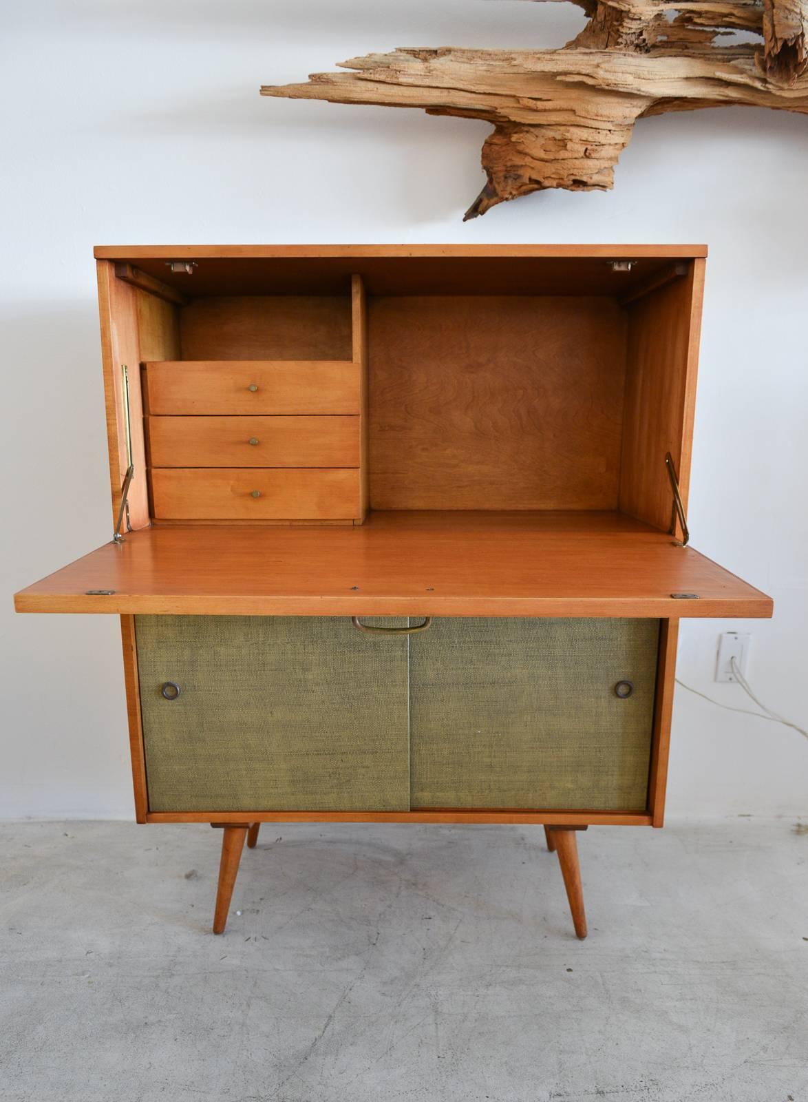 Paul McCobb secretary desk with grasscloth doors, circa 1955. Beautiful original condition, grasscloth is perfect with inner adjustable lower shelf and three upper drawers. Front folds down to reveal writing surface of approx. 34