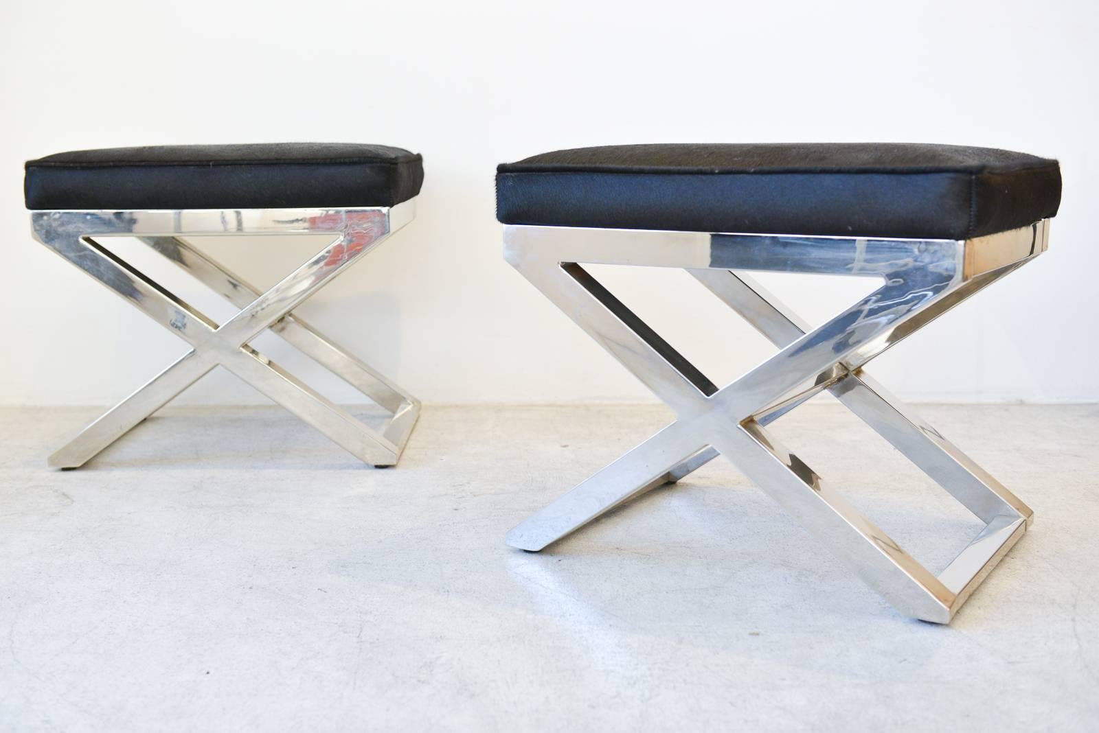 Beautiful pair of chrome X-base stools or benches with cowhide seats in the style of Milo Baughman. Newly upholstered in beautiful black cowhide for a great contract. Chrome is in good condition, has been polished. Very slight patina in corners,