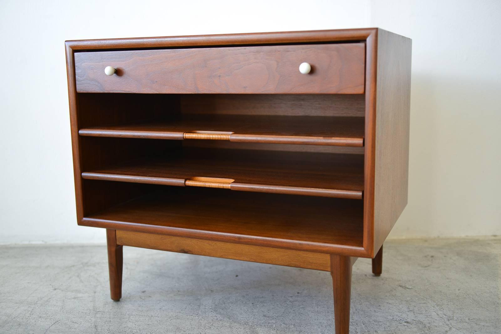Pair of Kipp Stewart Walnut Nightstands with Pull Out Magazine Shelves, ca 1965.  Professionally restored in showroom condition with cane wrapped shelves and original porcelain drawer hardware.  Drawers slide out easily and are also