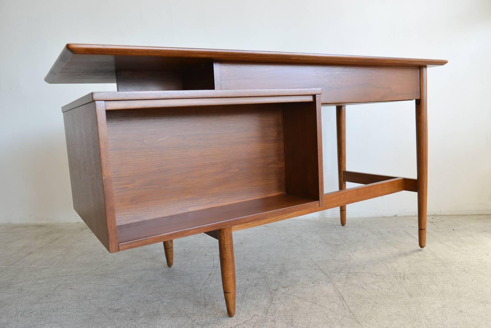 Floating top walnut desk by Hooker, circa 1965. Professionally restored in showroom perfect condition. Outer sliding door is reversible from walnut to cane. Inner sliding drawers and upper drawer for storage. Return (opposite) side is open for books