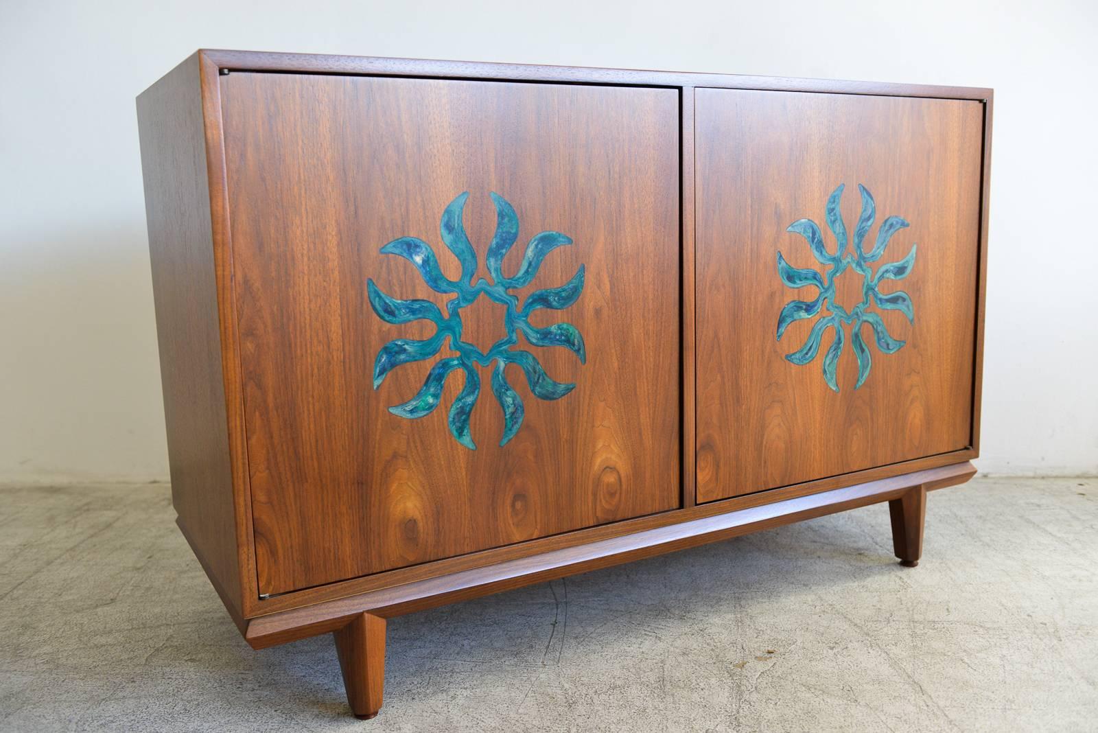 Walnut and enameled two-door dresser by Cal Mode, circa 1970. Professionally restored in showroom perfect condition. Beautiful green/blue enameled sunburst motif on front. Cabinet opens to reveal two adjustable inner shelves. Finished on the