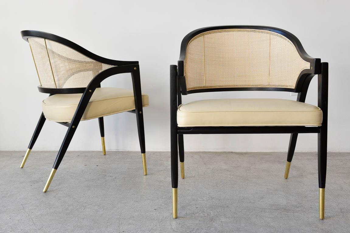 Edward Wormley for Dunbar style 5480 pair of sculpted armchairs, circa 1955. Fully restored, ebonized frames with new ivory leather upholstery and new cane backs. Beautiful brass detailing has been polished and shines with no rust. Rare, hard to