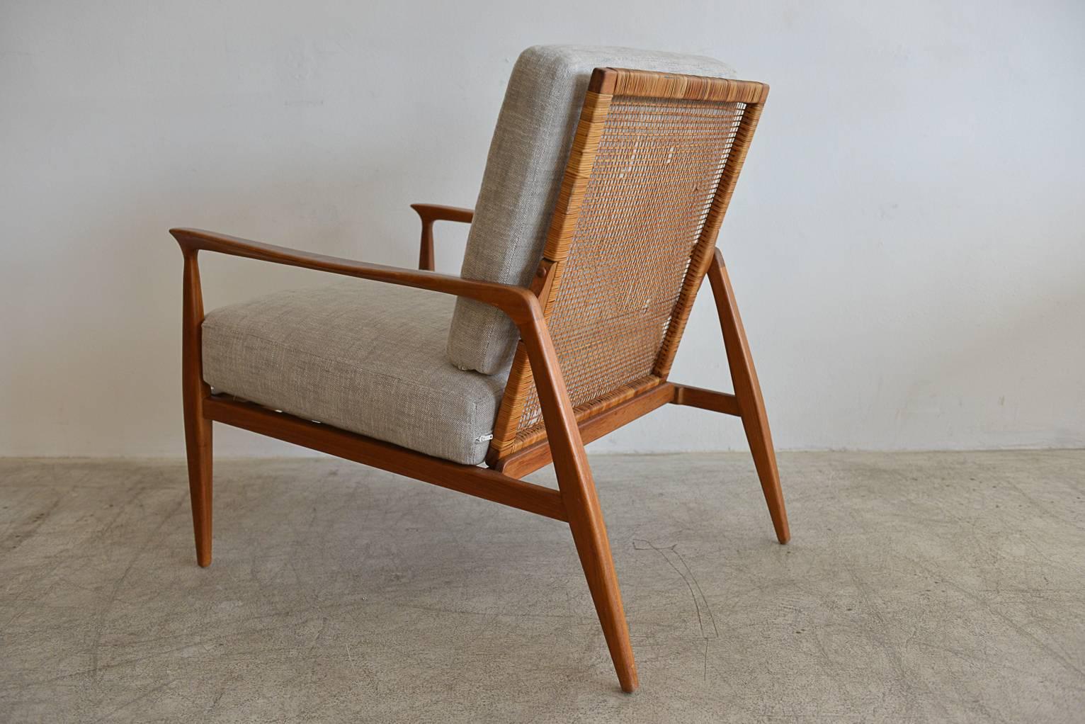 Teak and cane back lounge chair in the manner of Ib Kofod-Larsen. Beautiful lines, sculpted legs and armrests with great detail in the cane back.

New professionally restored cushions in neutral grey tweed with new foam. Cane back is in good