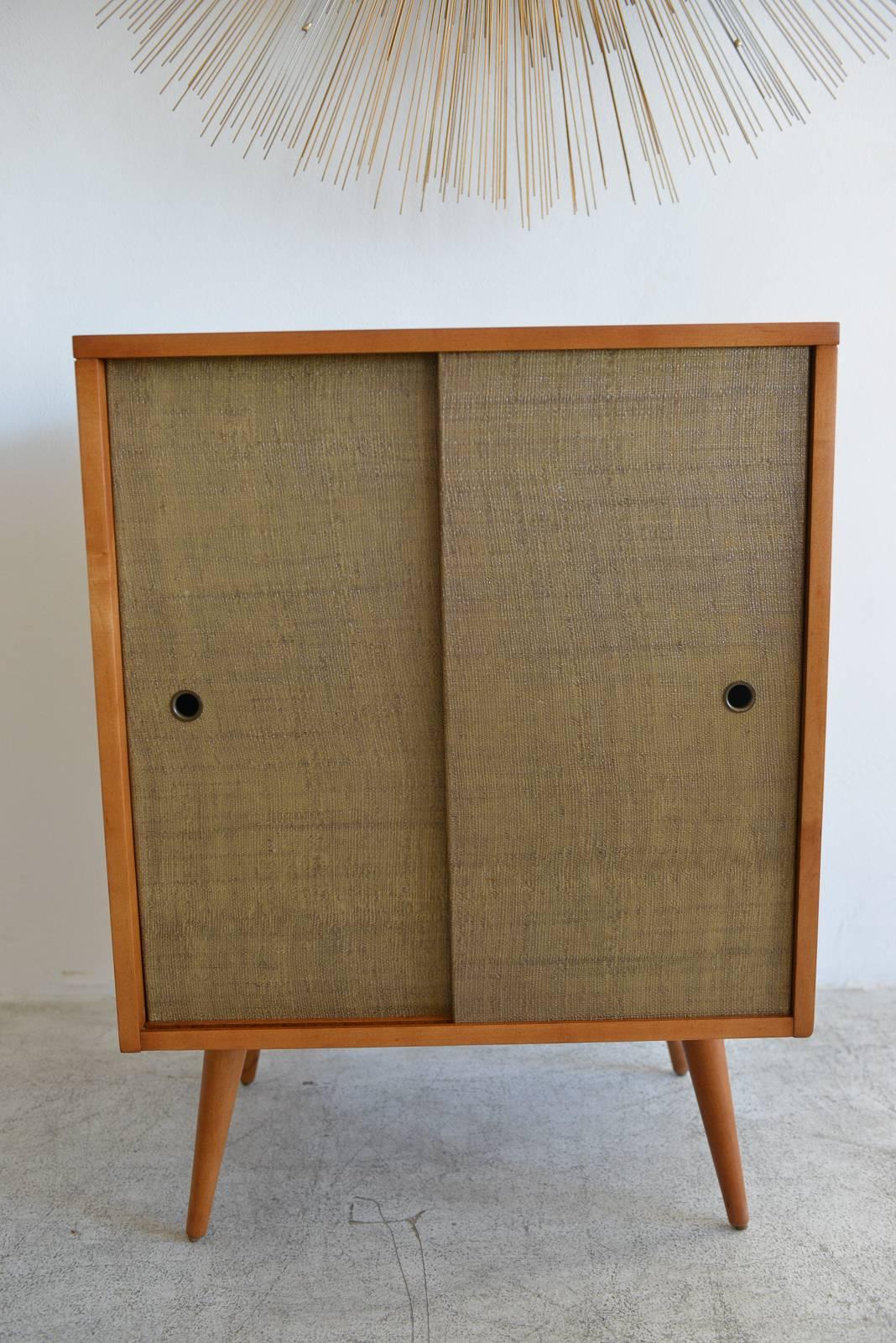 Paul McCobb planner group small cabinet, circa 1955. Maple with original grass cloth sliding doors. Perfect by itself or as a compliment to the larger cabinet available in a separate listing. Professionally restored wood in showroom