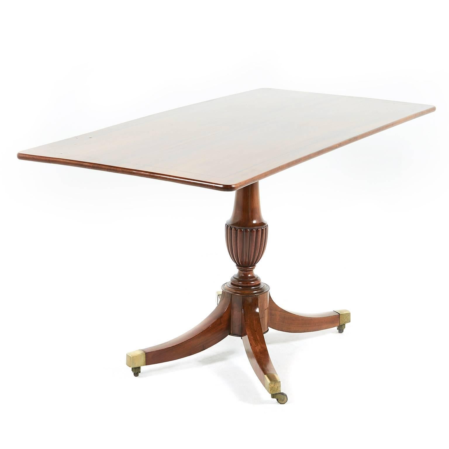 An antique English tilt-top breakfast table of unusually-narrow proportions. The top is comprised of solid Cuban mahogany with inlaid ebony stringing, standing on a pedestal base with out-swept ‘sabre’ legs terminating in original brass and leather