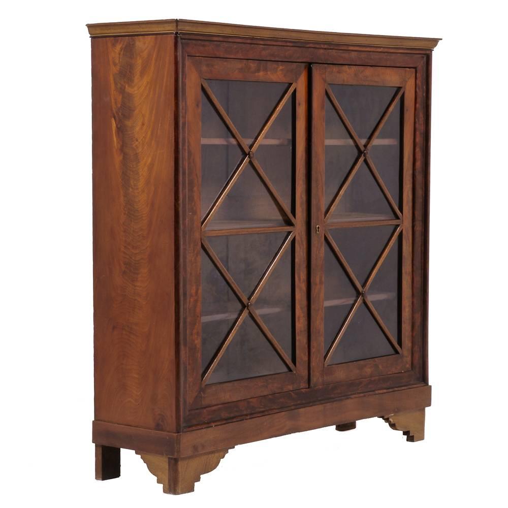 A simple French Empire two-door bookcase in mahogany, with adjustable shelves and cross-pattern to doors. 
Beautiful flame mahogany book-matched veneering to sides and door fronts.
