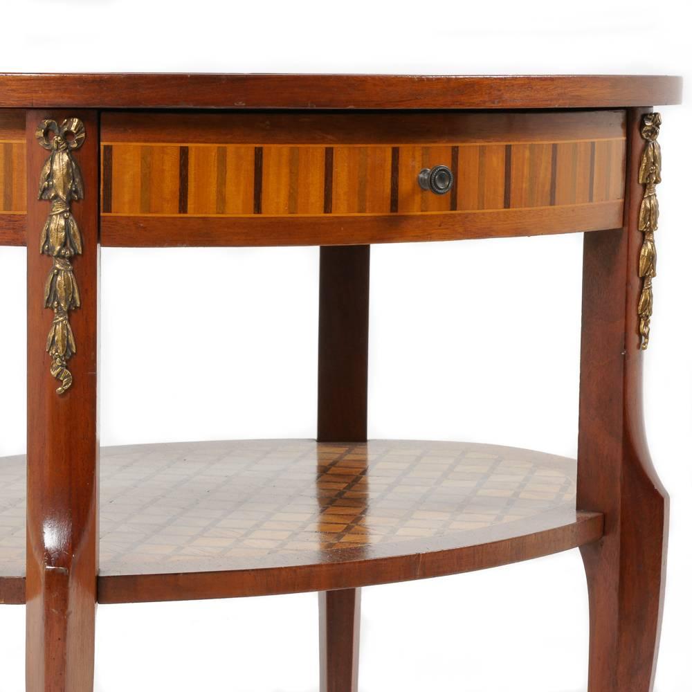 Lovely, rare, and smaller-scale oval, two-tier marquetry table from Paris. Early - Mid 20th Century French-made piece in excellent original condition. Gilt bronze mounts to sides and feet. One drawer.
