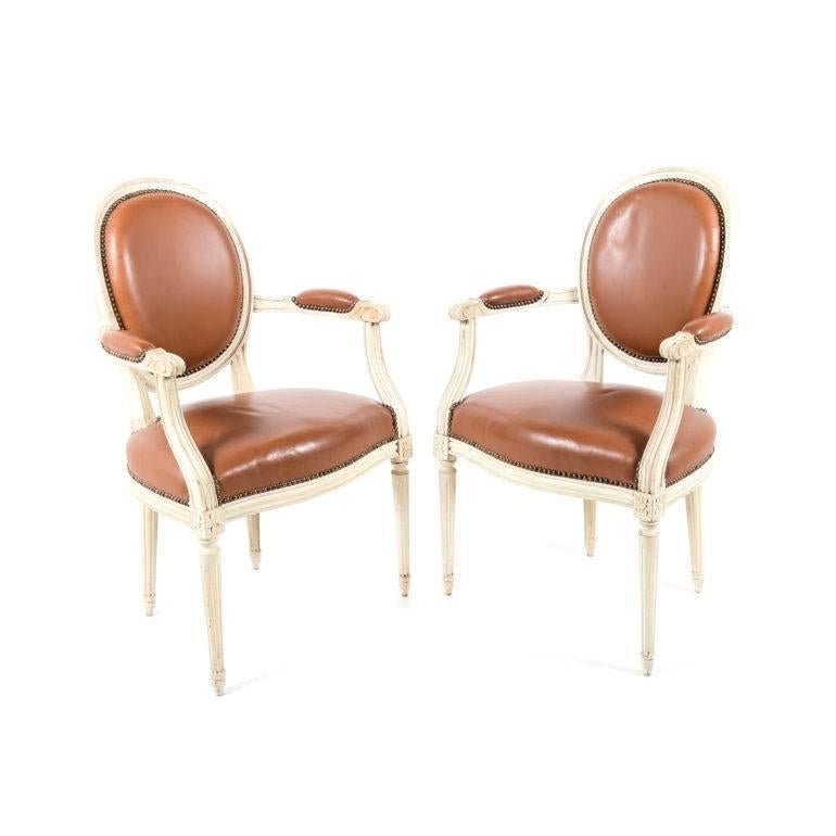 These are a lovely pair of original paint-and-leather Louis XVI armchairs from France. The leather is distressed, particularly on the seat itself, but perfectly usable. 
