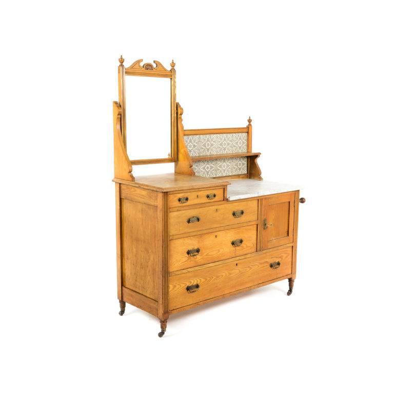A charming English Victorian ash dresser and washstand, having its original brass hardware, tiled back, marble, and mirror, circa 1880. Featuring four drawers of varying sizes as well as a cabinet and hanging rack, this cabinet would make a quaint