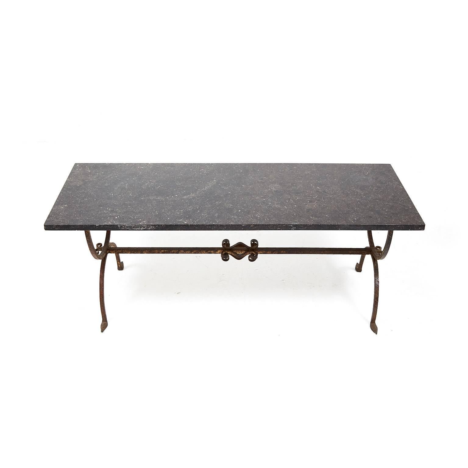 Antique French 1930s coffee table with wrought iron base and black granite top. Italianate curves on the support struts and a leaf design on the legs. The deep granite color contrasts nicely with the wrought iron. A solid and lovely piece suitable
