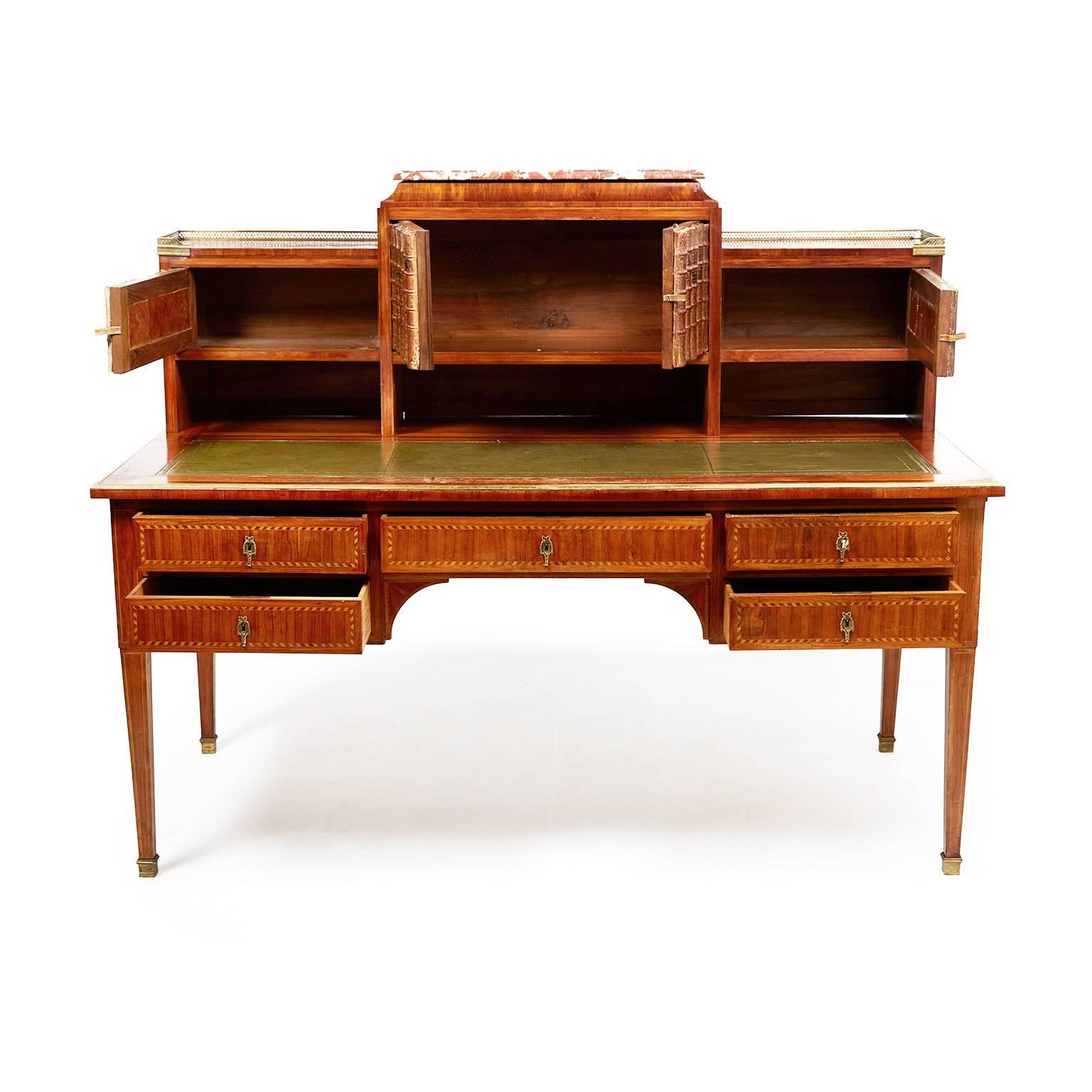 Superior quality 19th century, large French Louis XVI marquetry-and-inlay desk, with newly-replaced leather surface and 18th century book spines fronting the cupboard doors. With subtle brass accents, and crowned with a beautiful piece of marble,