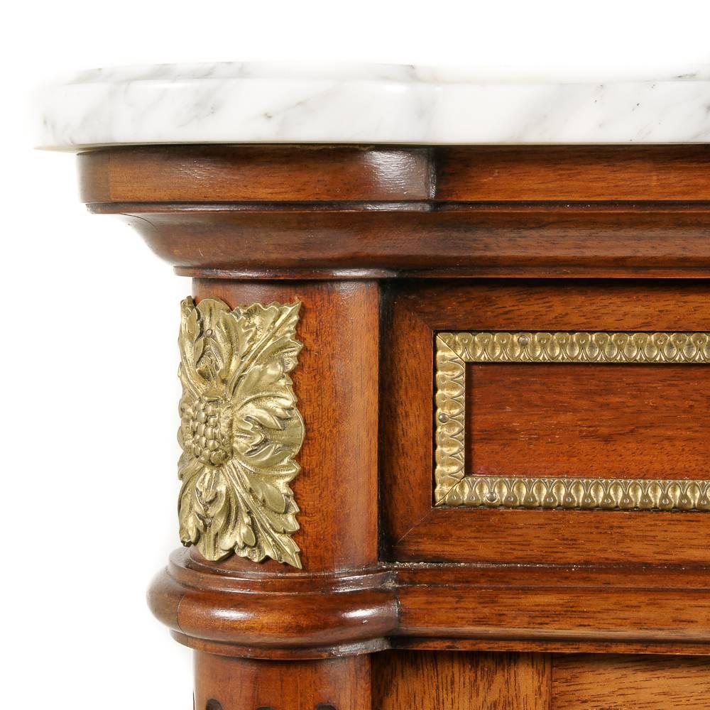 A very nice-quality French Louis XVI-style marble-top cabinet in mahogany, the two doors enclosing glass display shelves with lower hidden storage.

The piece features a shaped top of Carrera marble, and finely cast and finished gilt mounts to