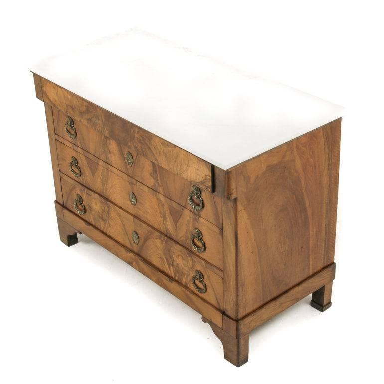 Gorgeous Empire style French marble-top commode, with four drawers; in figured walnut, circa 1860. The deep, rich tones of the walnut are beautifully offset by the cream-white colour of the marble and the striking brass accoutrements.



     