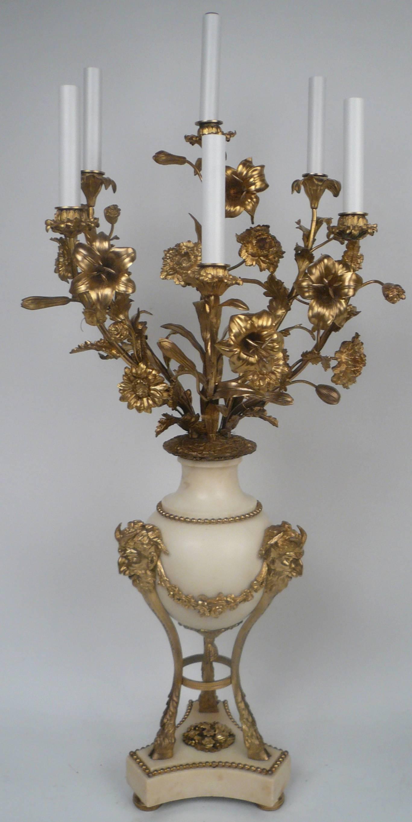 This imposing pair of neoclassical style candelabra feature naturalistic floral branches. The urn form bases of Carrara marble, are on tripod hoofed feet and have satyr masks and swaged floral garland decoration.