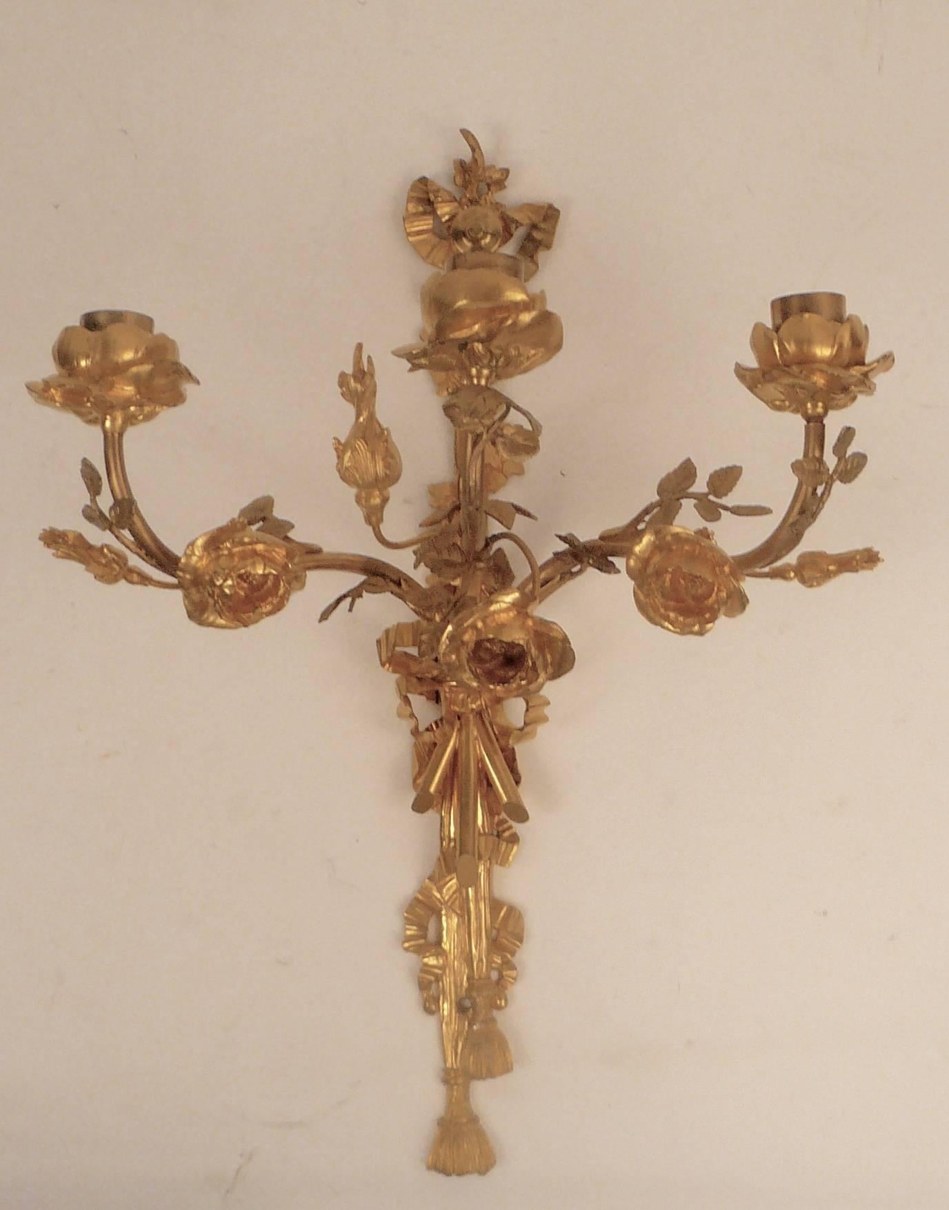 This pair of floral three arm gilt bronze sconces feature finely cast roses, bowknots, and tassels.