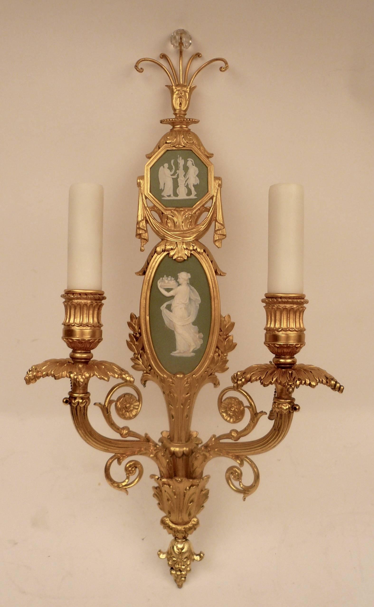 This impressive pair of two-light sconces feature wedgwood jasperware plaques mounted in gilt bronze.