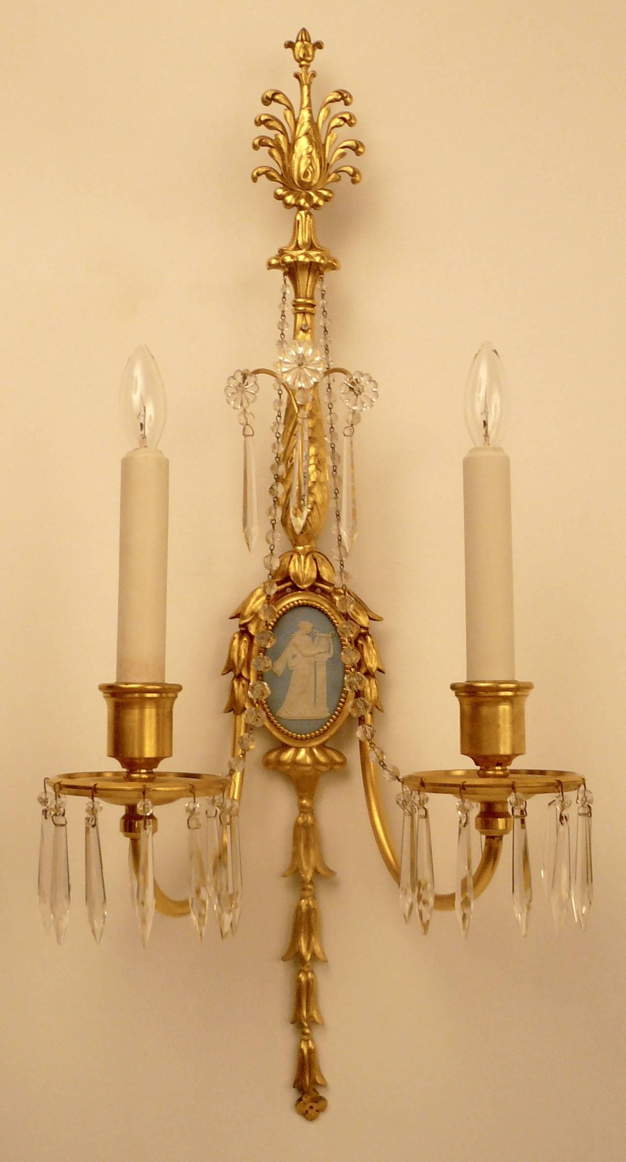 This quality pair of neoclassical style two-light gilt bronze sconces are finely cast with hand chased details. They are mounted with signed Wedgwood jasper ware plaques in the style of Robert Adam.